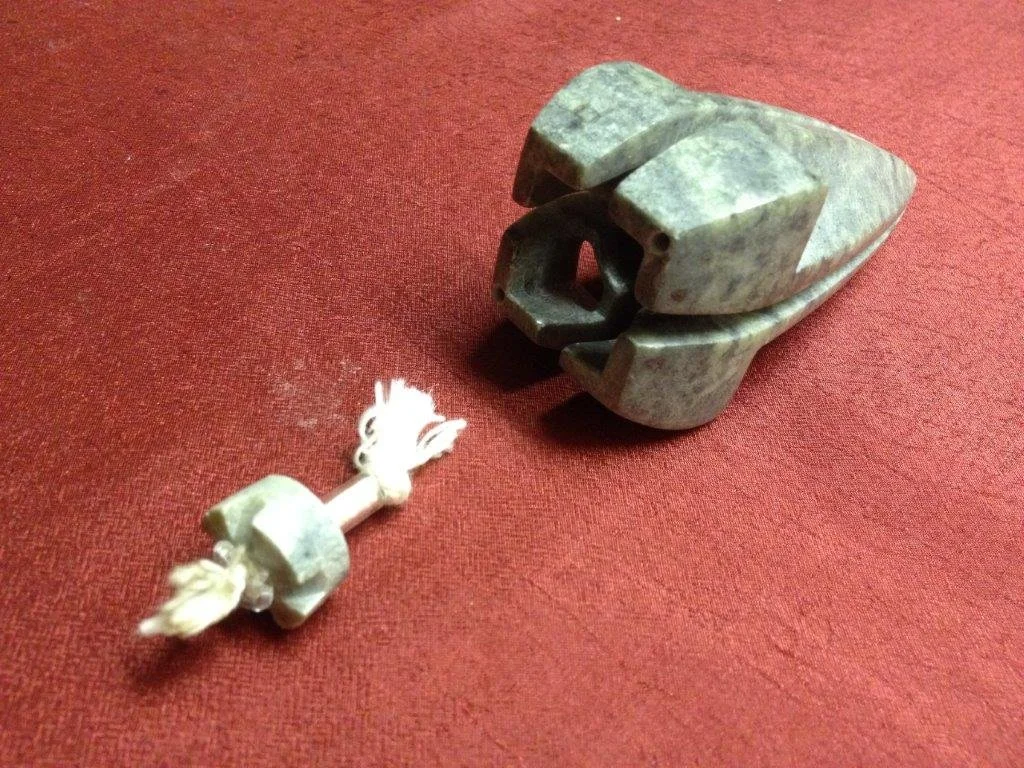 Eine kleine Schampe mit Schnur liegt vor einem großen Krokodil aus Stein auf einem roten Hintergrund.