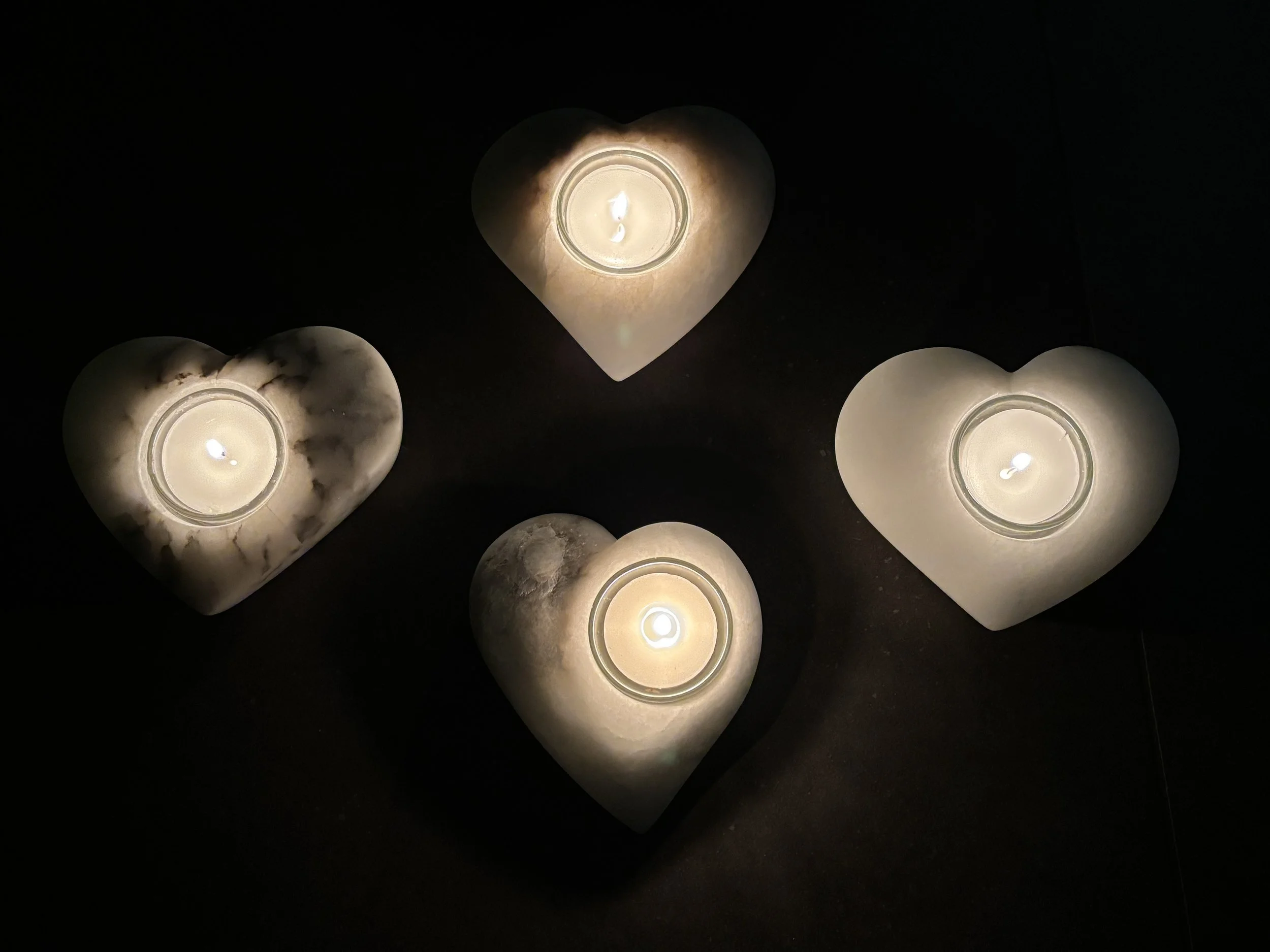 Fünf ausgeleuchtete Kerzen in Herz-Formen auf einem dunklen Hintergrund.