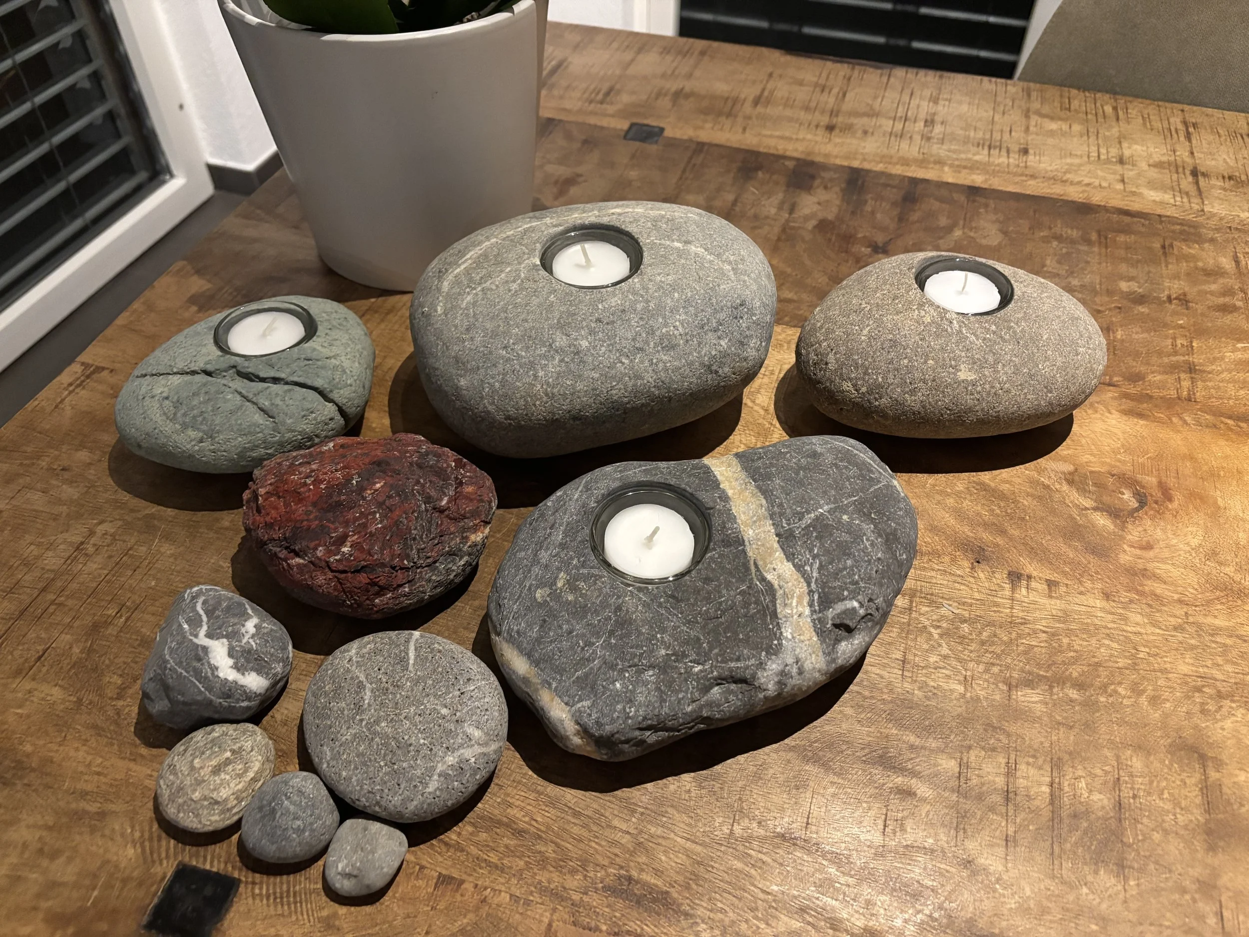 Verschiedene Steine mit Teelichtern auf einem Holztisch.