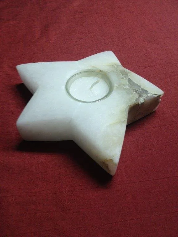 Ein weißes Sternförmiges Kerzenhalter aus Marmor mit einer Kerzenschneid für eine Teelichtkerze, liegt auf einem roten Holztisch.