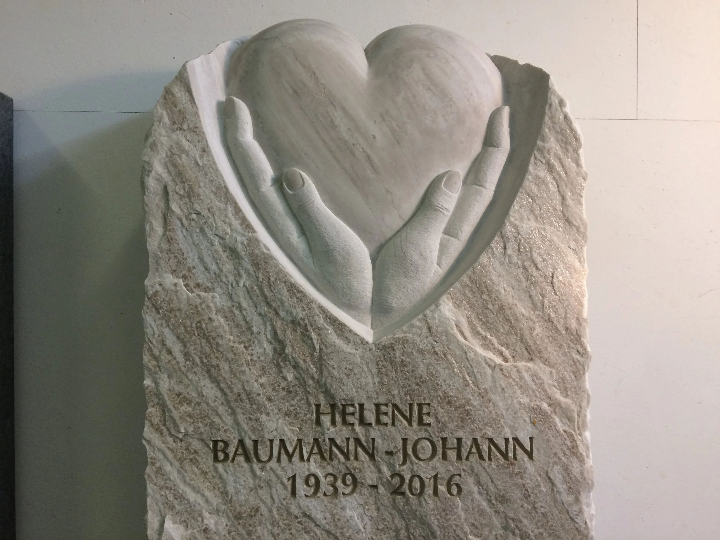 Grabstein mit einem Relief einer Hand, die ein Herz hält, und der Inschrift: Helene Baumann-Johann 1939-2016.