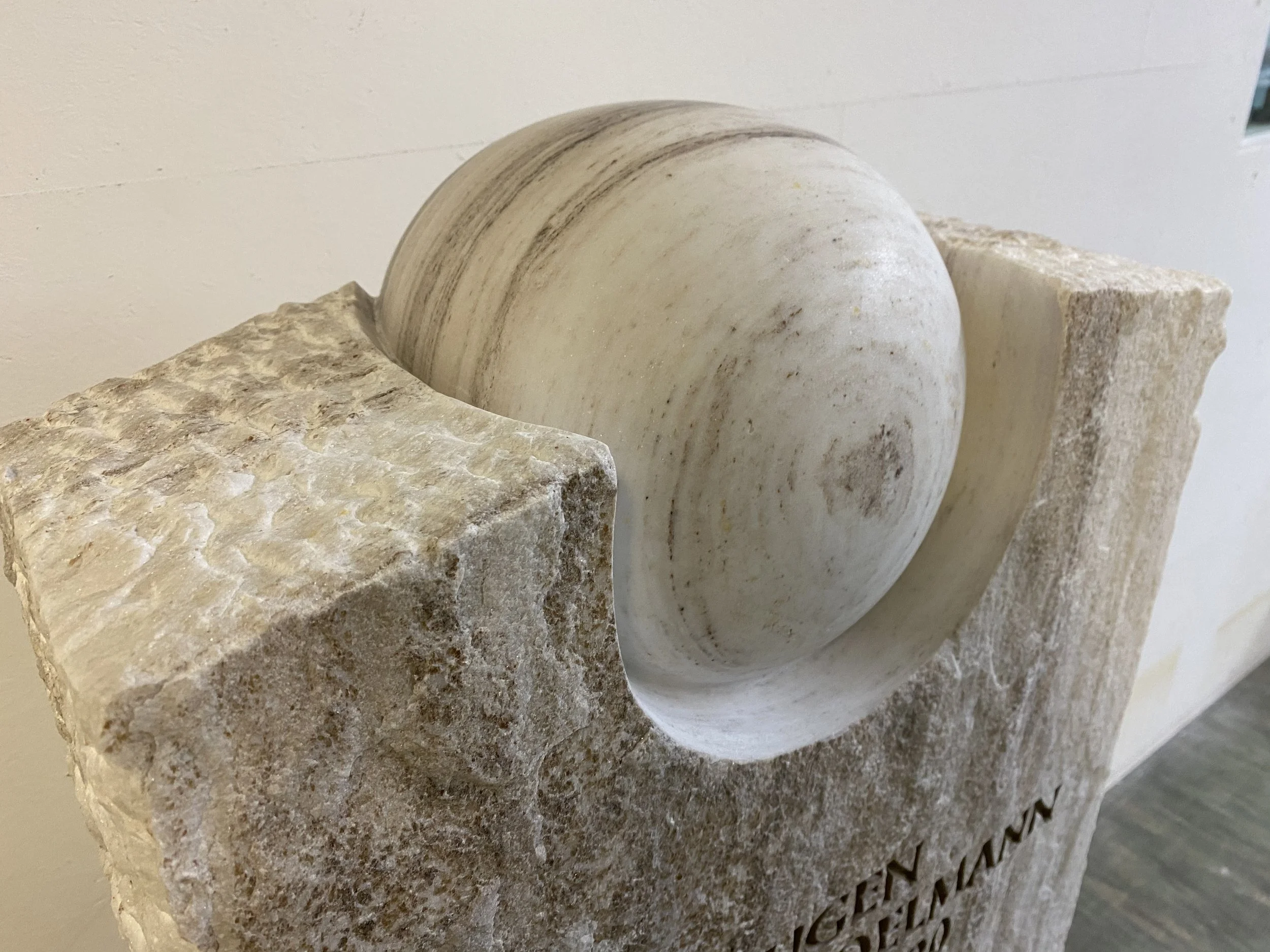 Ein kunstvoll gestaltetes Skulptur aus Muschelkalk mit einer runden, spiralförmigen Muschel in der Mitte, umgeben von porösem Stein.