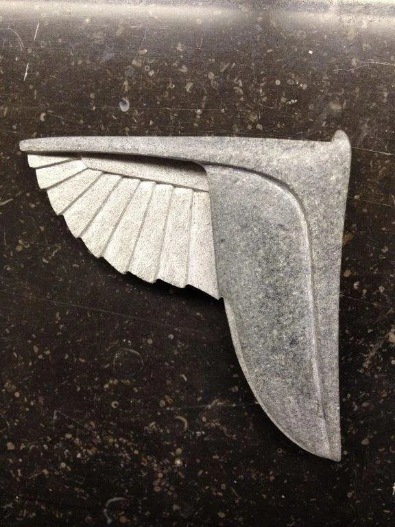 Metallstück in Form eines Winkel- oder Halterarmteils mit geriffeltem Arm auf einer dunklen, speckigen Oberfläche.