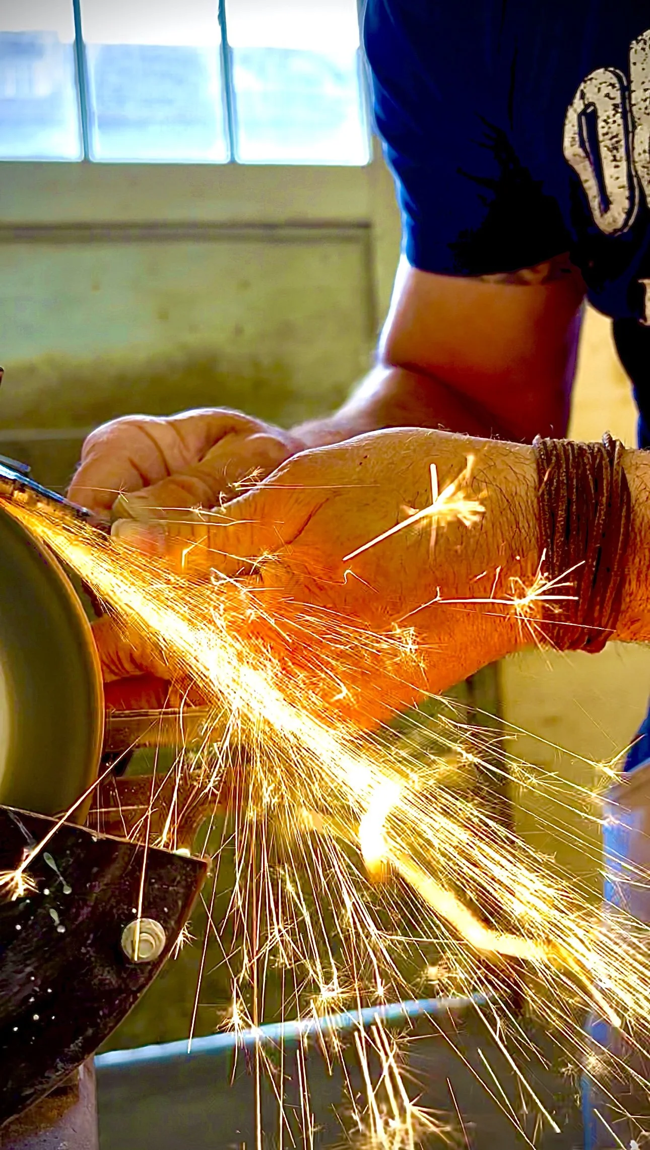 Ein Handwerker schweißt Metall und erzeugt dabei zahlreiche funkenartige Lichtblitze in einem Werkstattumfeld.