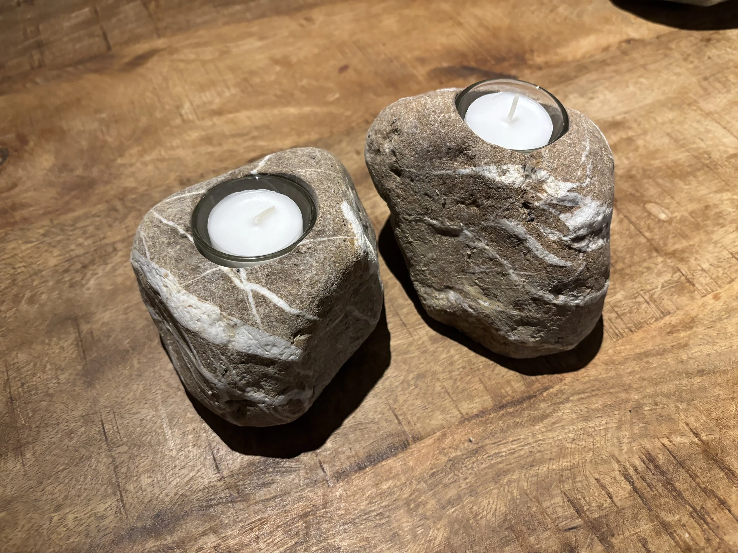 Zwei Steine mit Teelichtern in Kerzenhaltern auf einem Holztisch.