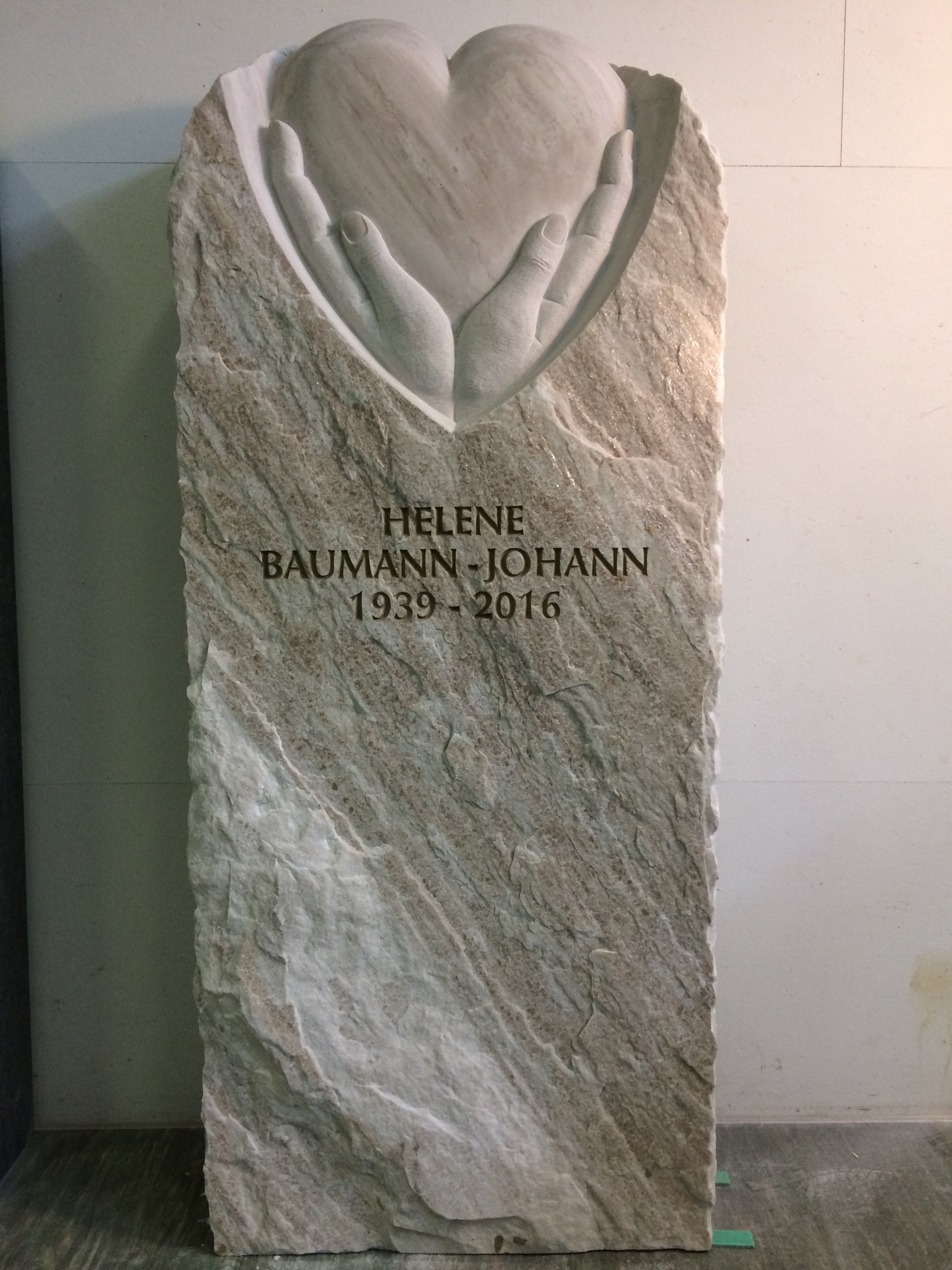 Grabstein mit einem Relief von zwei Händen, die ein Herz halten, darunter die Inschrift: HELENE BAUMANN-JOHANN 1939-2016.