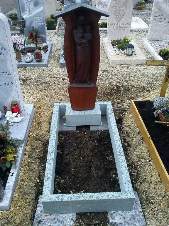 Gräber im Friedhof mit einem Holzkreuz und einem Grabrahmen aus Stein, das Grab ist noch unbestattet.