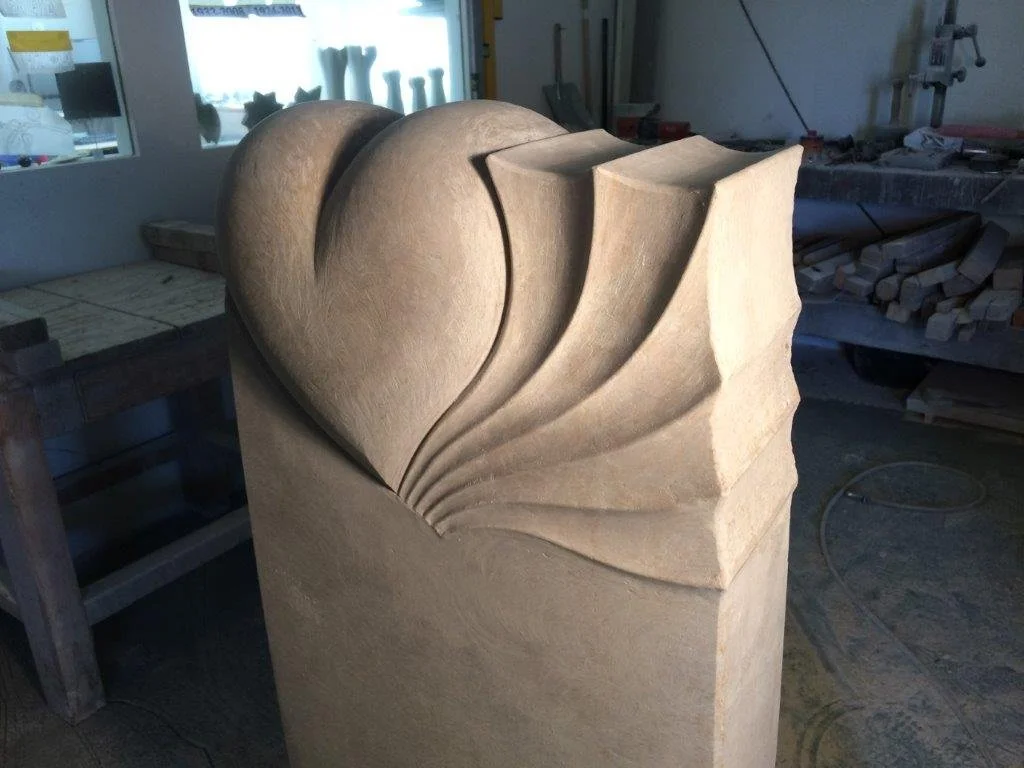 Sandstein-Skulptur in Form eines Herzens mit mehreren geschwungenen, wellenförmigen Linien in einem Kunst- oder Werkstattstudio.