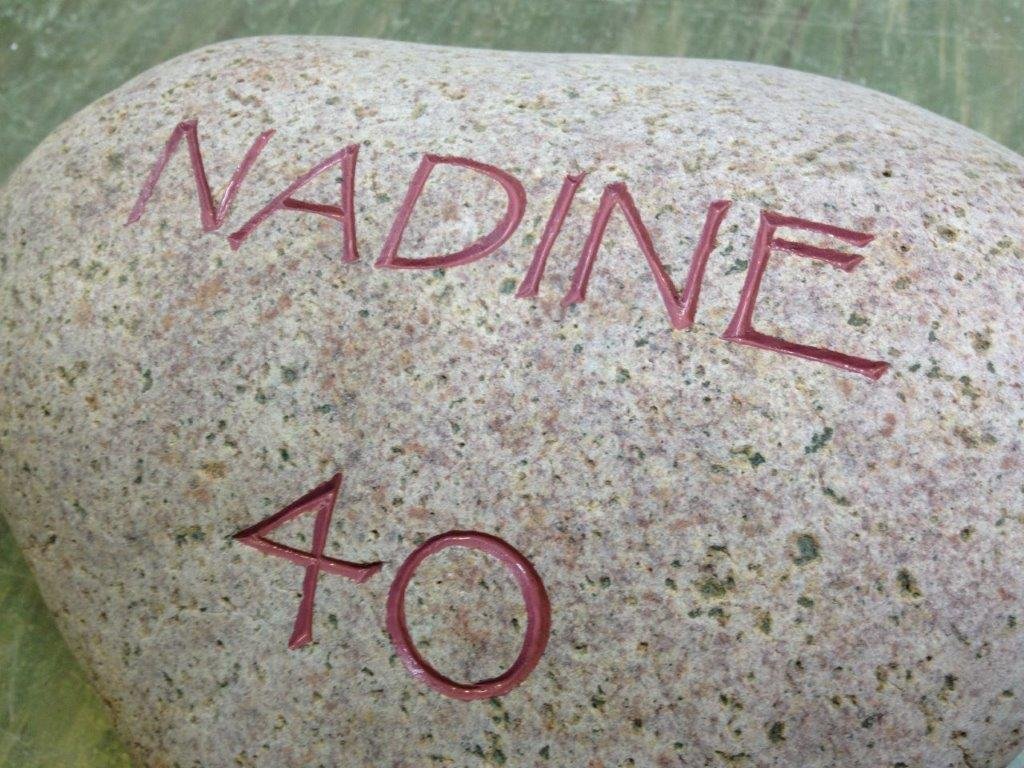 Ein großer, glatter Stein mit handgeschriebenem Wort 'NADINE' und der Zahl '40' in roter Farbe.