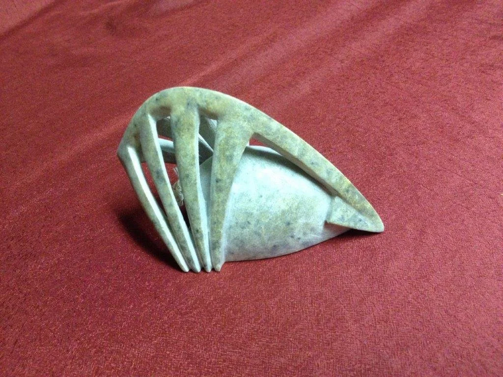 Ein kleiner, geschnitzter Edelstein oder Knochen mit einer in den Stein geschnitzten modernen, abstrakten Skulptur. Es liegt auf einem roten Stoffhintergrund.