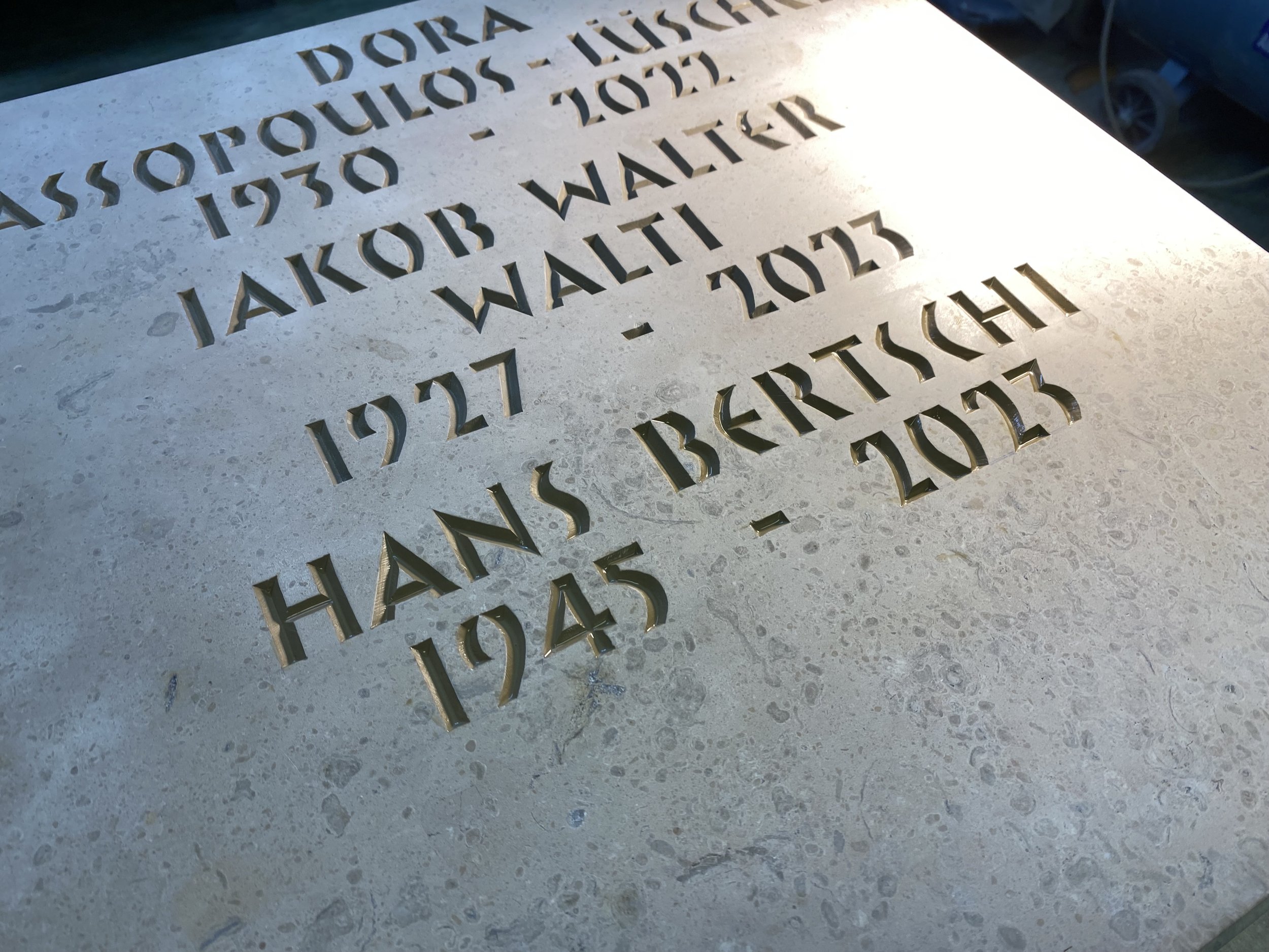 Gedenkstein mit historischen Daten und Namen, teilweise vom Sonnenlicht beleuchtet