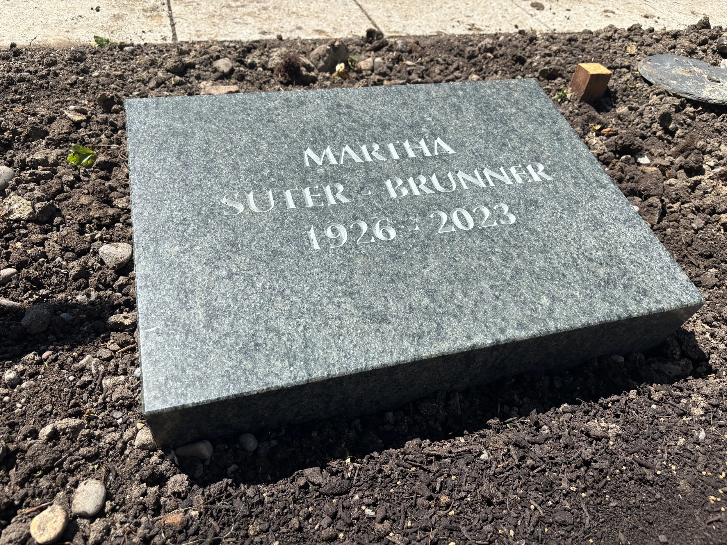 Grabstein mit Namen Martha Suter- Brunner und den Jahren 1926 bis 2023, auf Erde liegend.