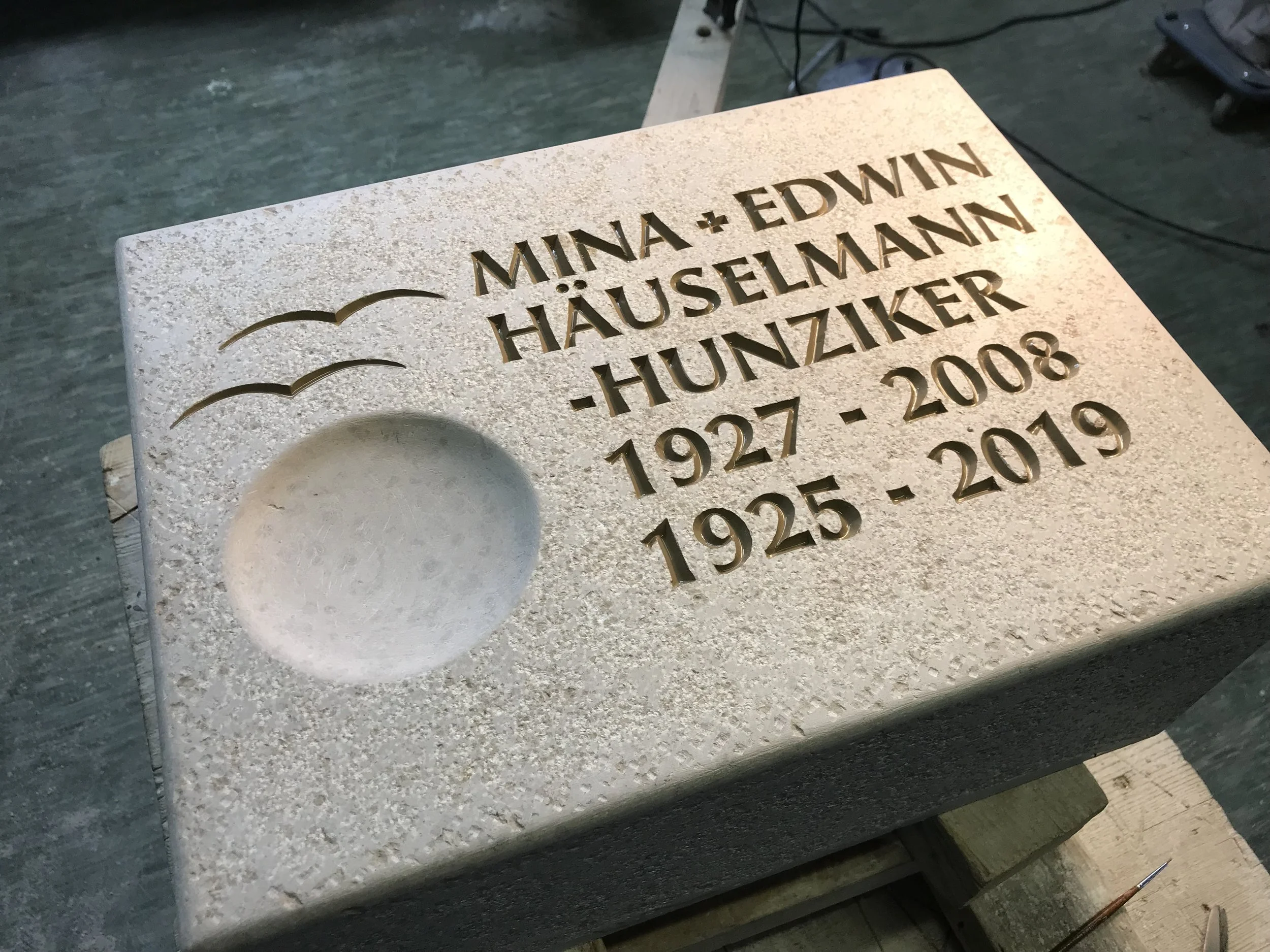 Gedenktafel aus Stein für Minna und Edwin Häuselmann, Hausierer und hunziker, mit den Jahren 1927-2008 und 1925-2019, auf einer Werkbank im Workshop.
