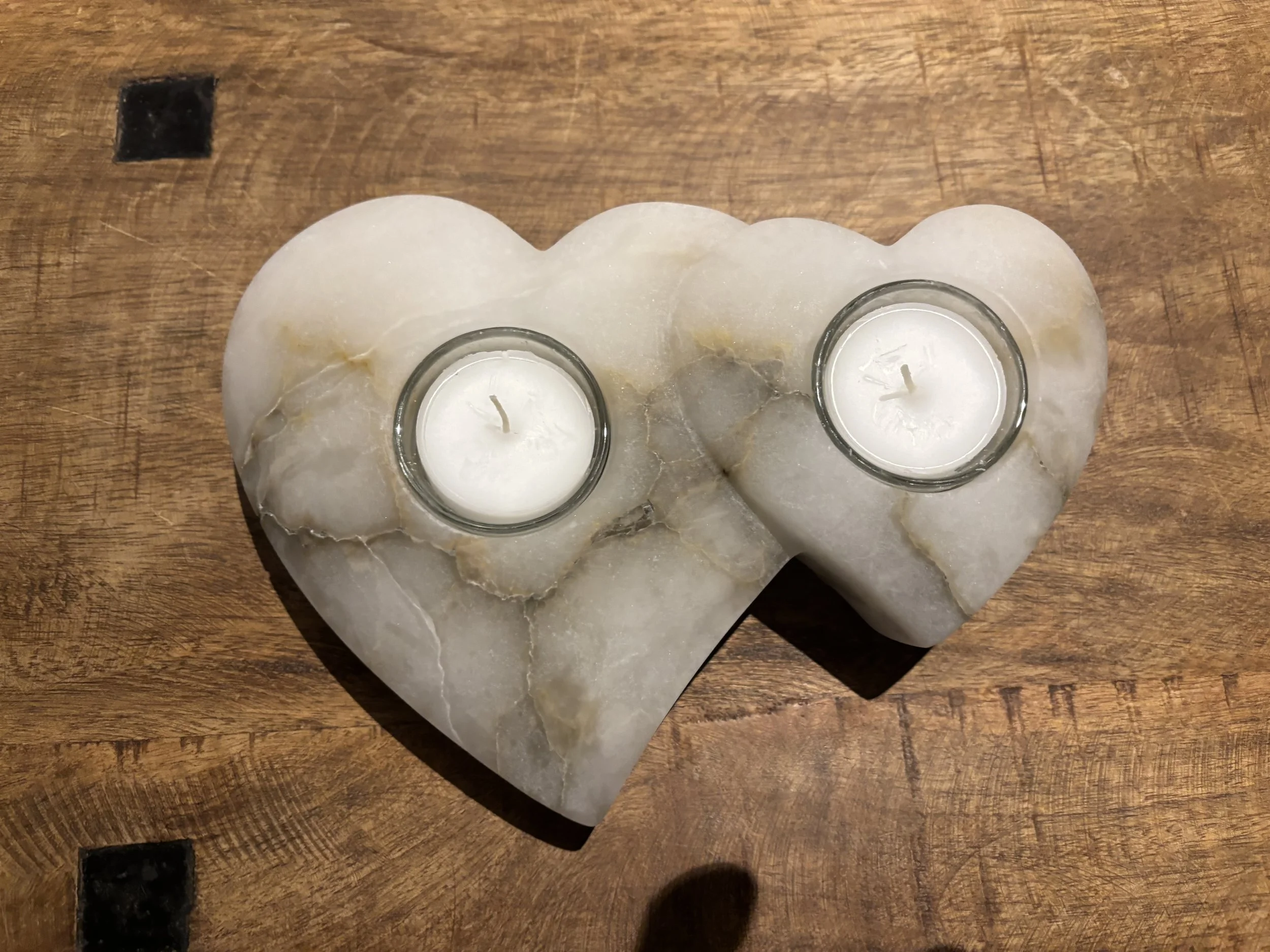 Herzförmige Dekoration mit zwei Kerzen in Gläsern auf einem Holzoberfläche.