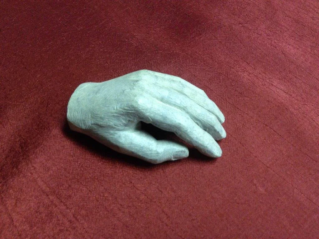 Eine weiße, Holzähnliche Handenskulptur liegt auf einem roten Stoffhintergrund.