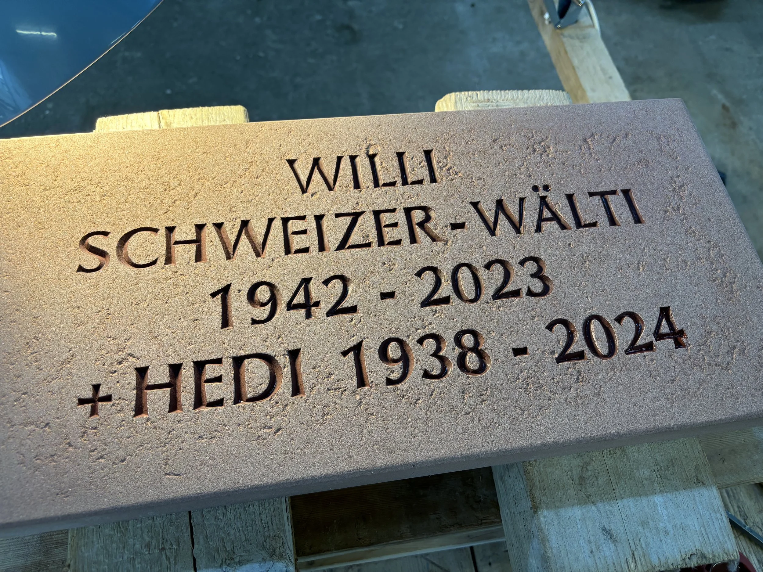 Gedenktafel für Willi Schweizer-Wälti und Hedi, mit Geburts- und Sterbedaten, auf einer Holzständer