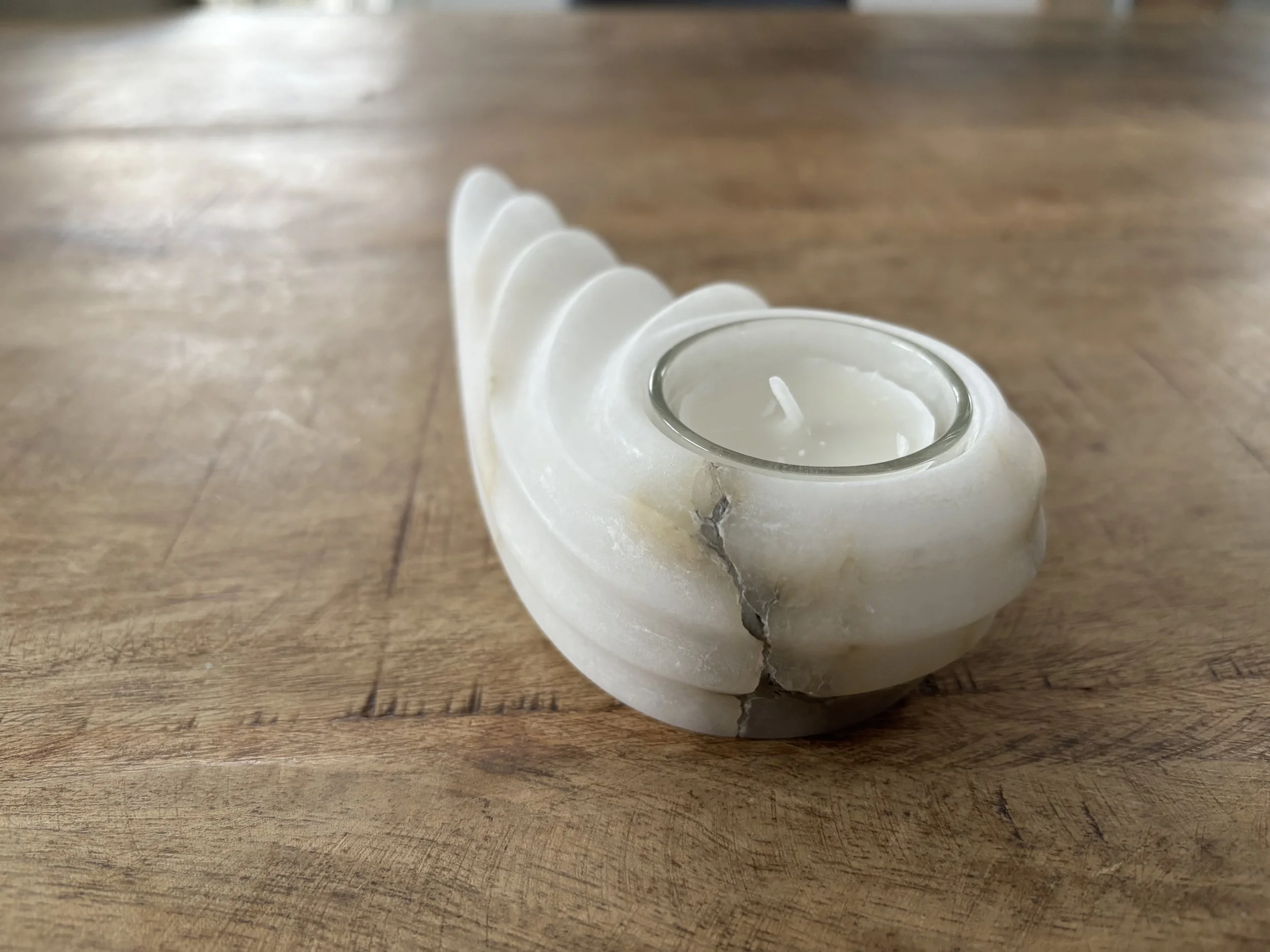 Eine weiße Kerze in einer Muschel auf Holztisch.