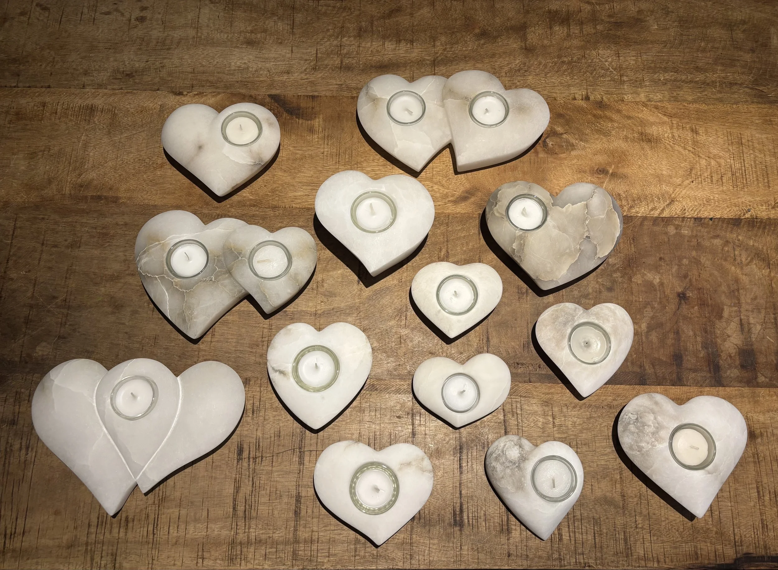 Mehrere Herzförmige Kerzenhalter aus weißem oder grauem Stein mit kleinen Kerzen, auf einem Holztisch