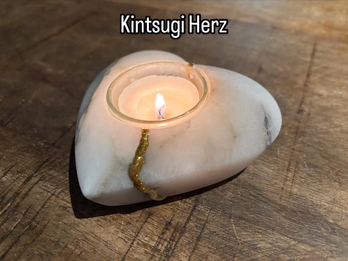 Kerze in einer weißen Steinhalterung auf einem Holztisch, mit goldener Dekoration