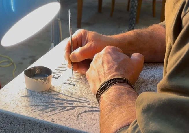 Eine Person graviert auf einem Stein oder einer Platte mit einem kleinen Werkzeug.