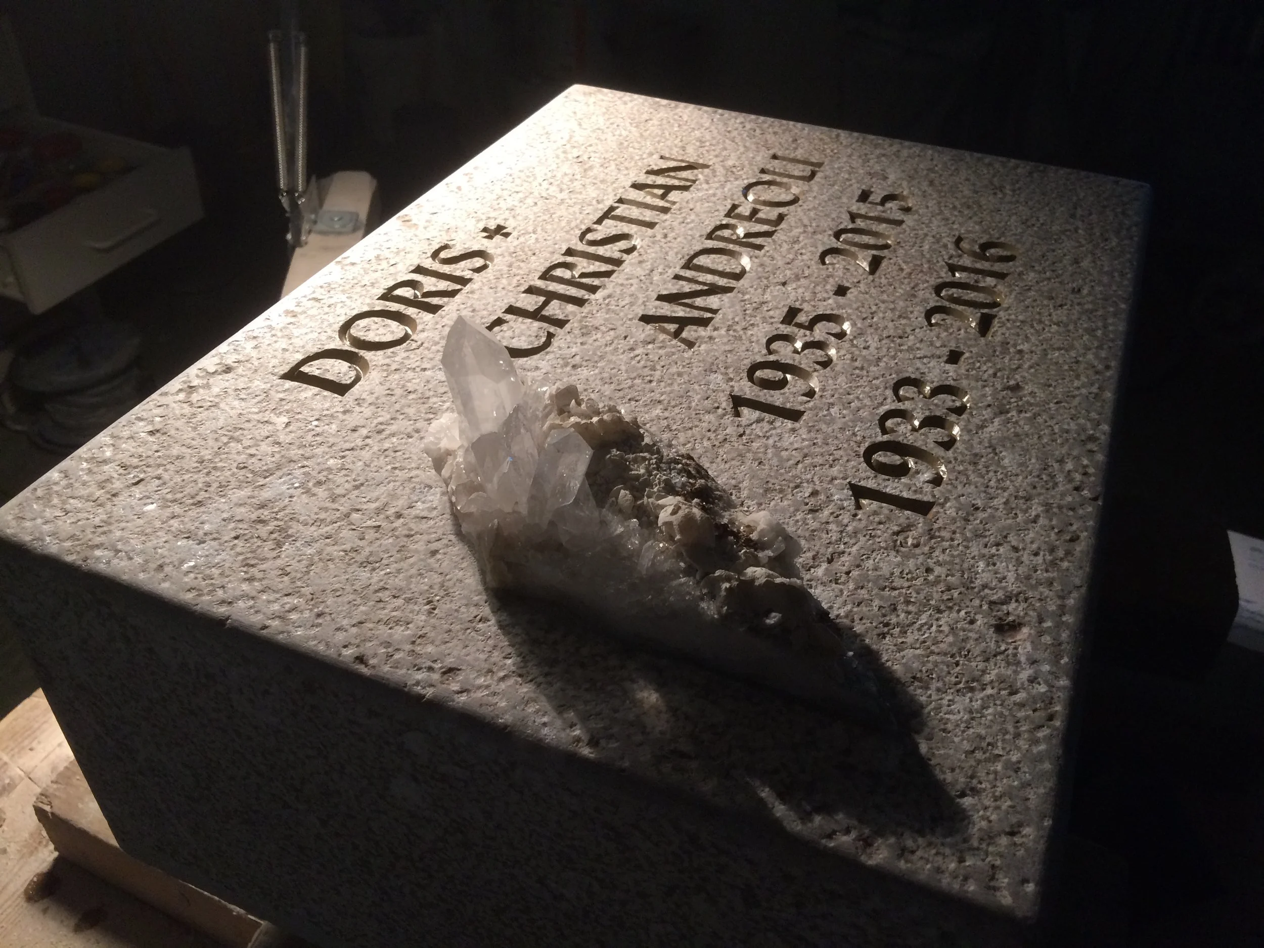 Granitstein mit eingravierten Namen, Daten und einer klaren Kristall auf der Oberfläche.