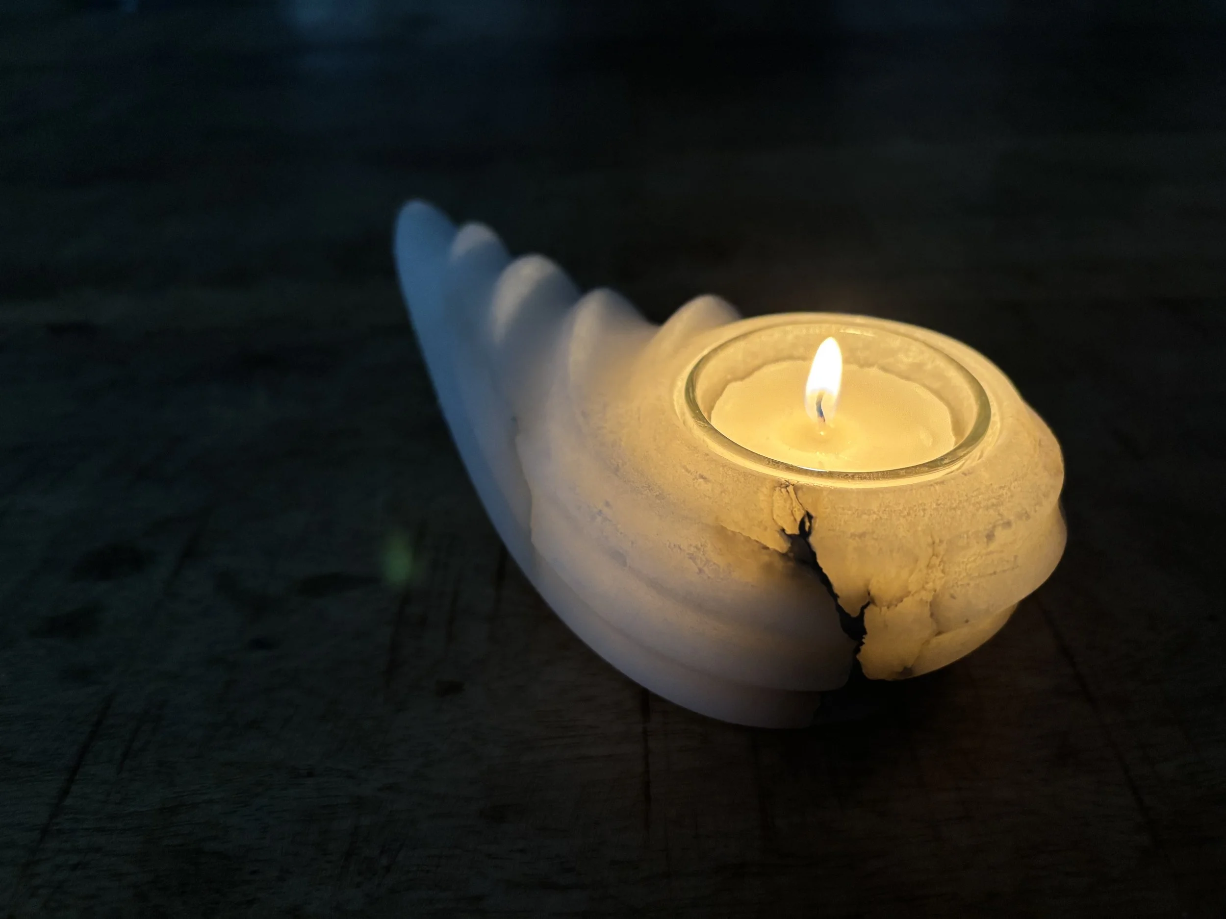 Ein brennendes Kerzenlicht in einer Schale, die auf einem dunklen Holzfußboden steht.