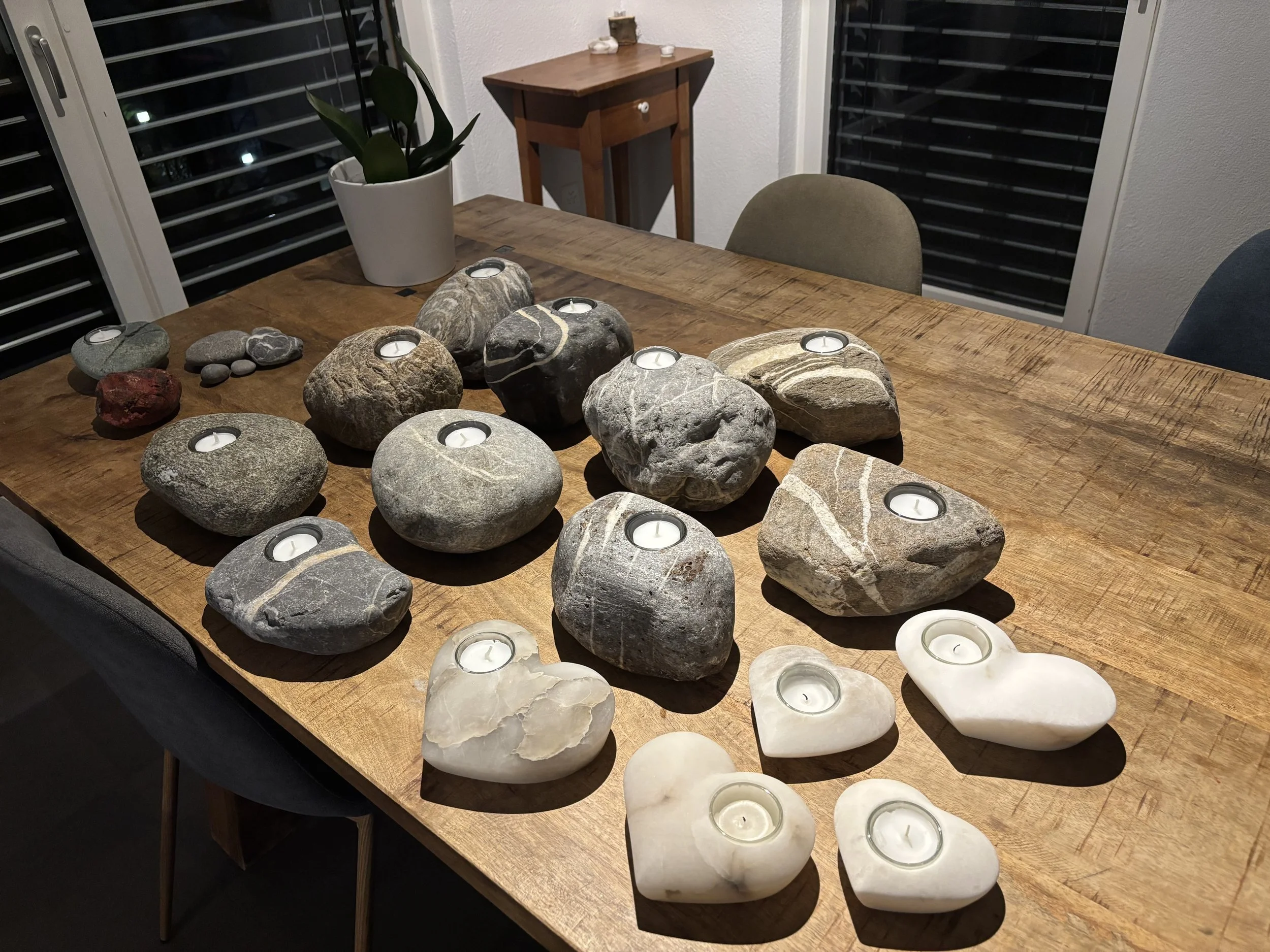 Steine in verschiedenen Formen und Größen, die als Kerzenhalter dienen, auf einem Holztisch, beleuchtet durch die Kerzen.