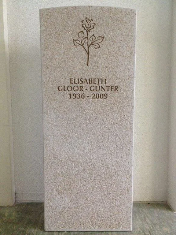 Grabstein mit einer stilisierten Rose oben, der den Namen Elisabeth Gloor-Günter und die Lebensdaten 1936-2009 trägt.