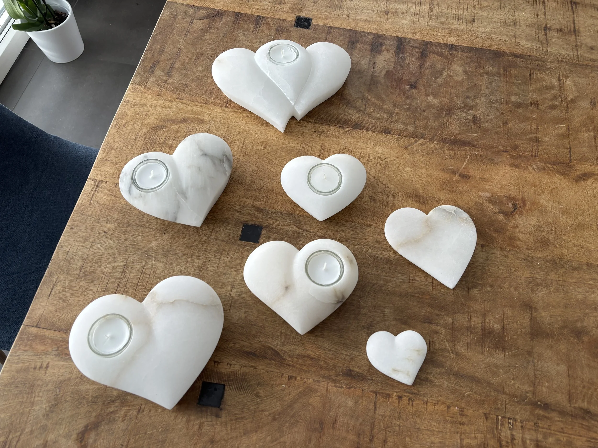 Sechs Herzförmige Kerzenhalter aus weißem Marmor auf einem Holztisch, einige mit einer kleinen Kerze darin.
