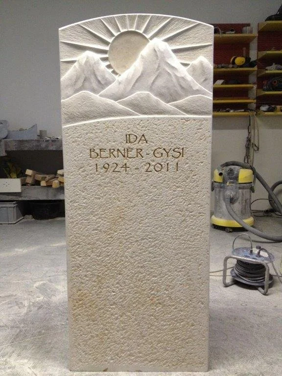 Stein mit eingelegter Gravur eines Bergmotivs mit Sonnenstrahlen und einer Inschrift.