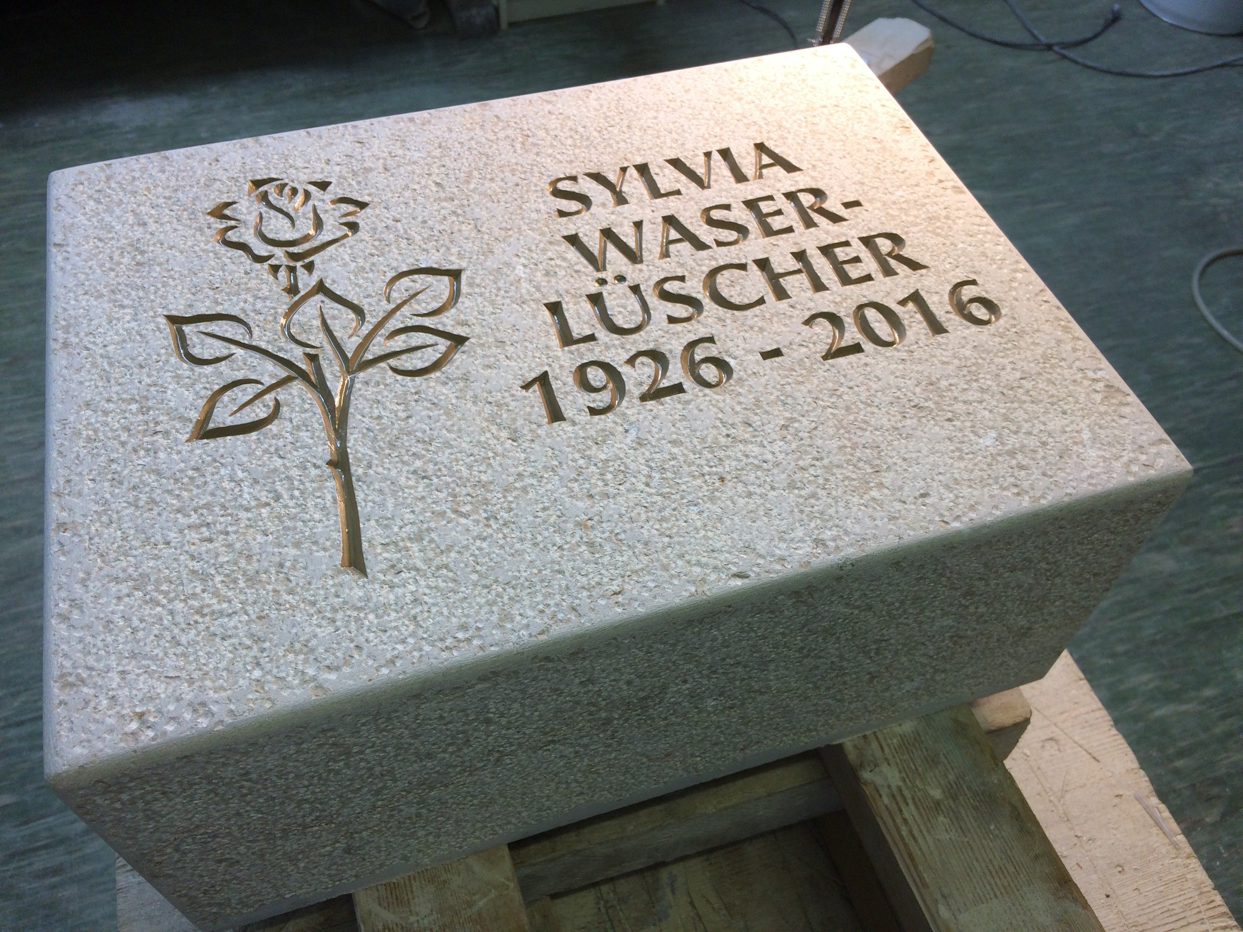 Grabstein mit eingekerbtem Rosenmotiv und der Inschrift: Sylvia Wasser-Lüischer, 1926-2016.