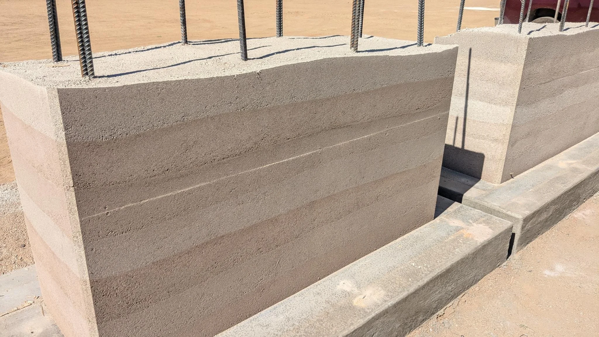 A close-up of a rammed earth wall with reddish-brown earth and mortar lines.