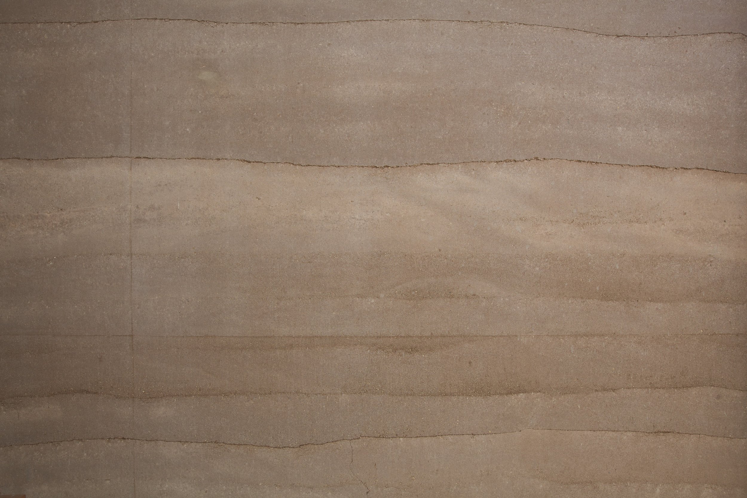 A close-up of a rammed earth wall with reddish-brown earth and mortar lines.