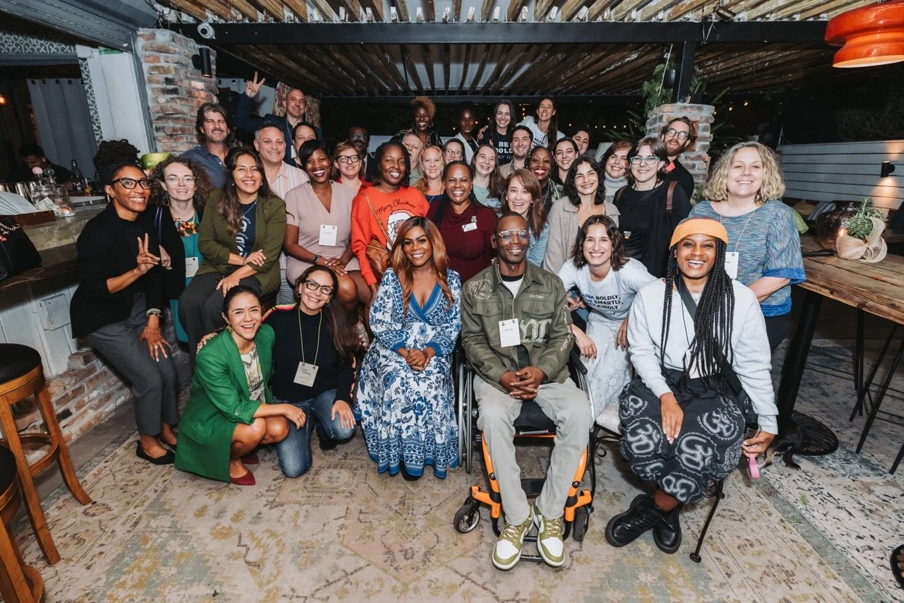 A group of diverse people gathered indoors for a group photo, smiling and posing together.