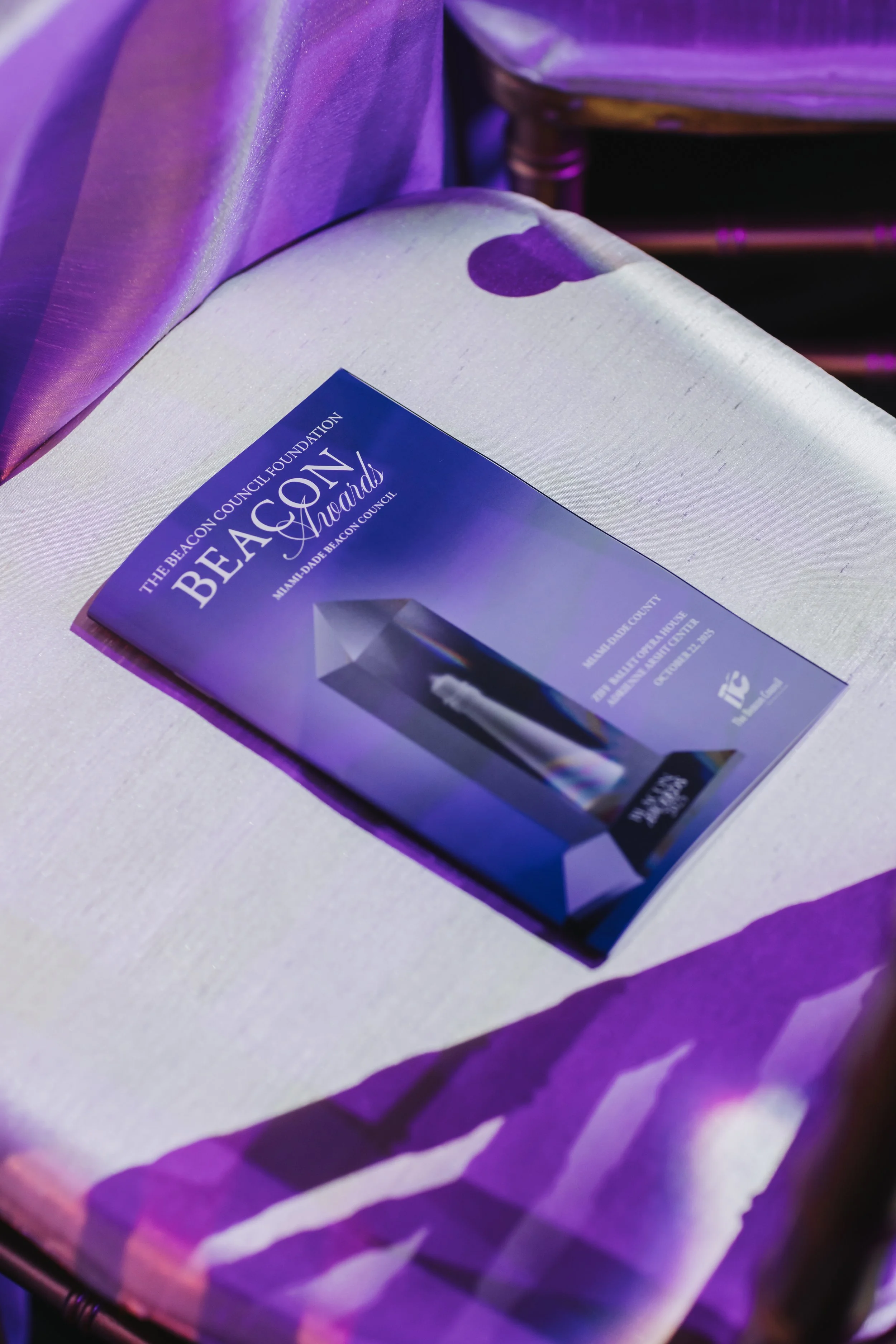 Invitation or flyer for the Miami-Dade Beacon Council Awards event, featuring a tall, modern, reflective award trophy with purple background.