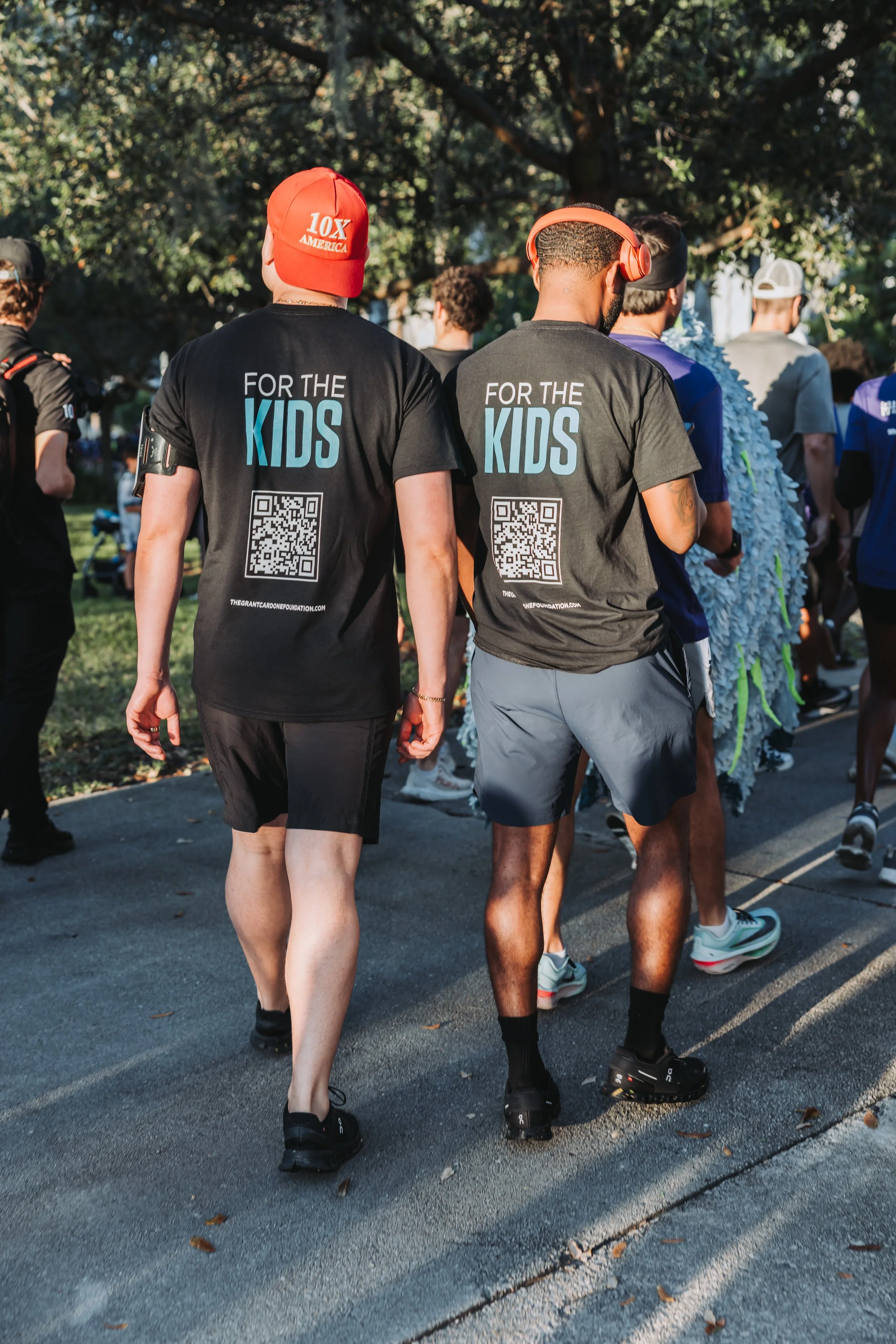 Two people are walking outdoors during a run or walk event, wearing black T-shirts with 