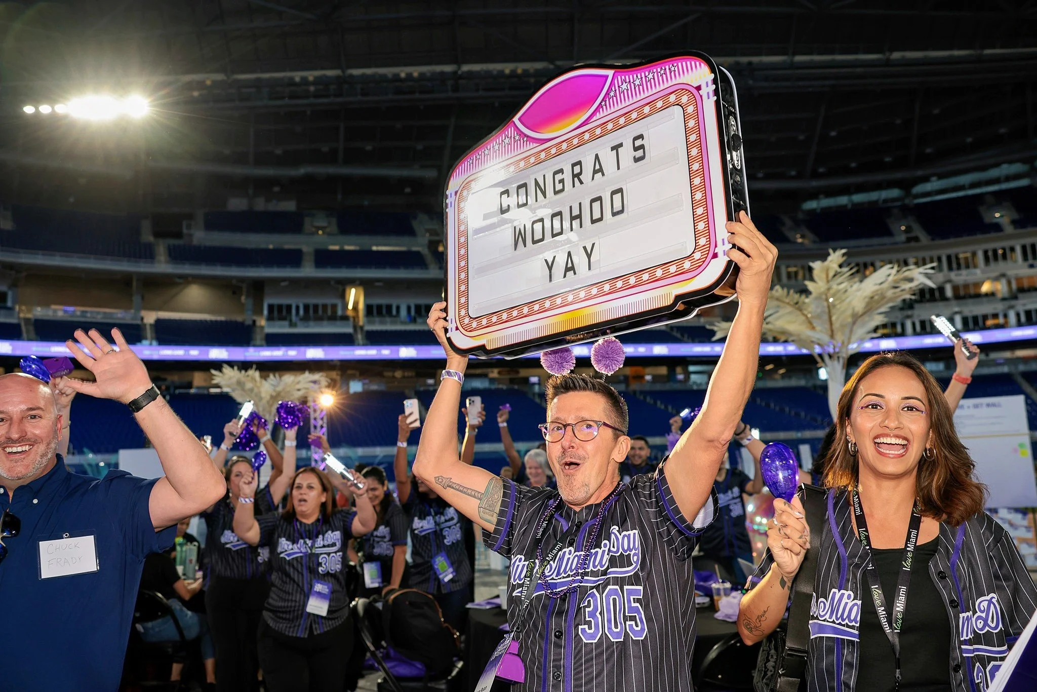 People celebrating at a stadium with a sign that says "Congrats WooHoo Yay."