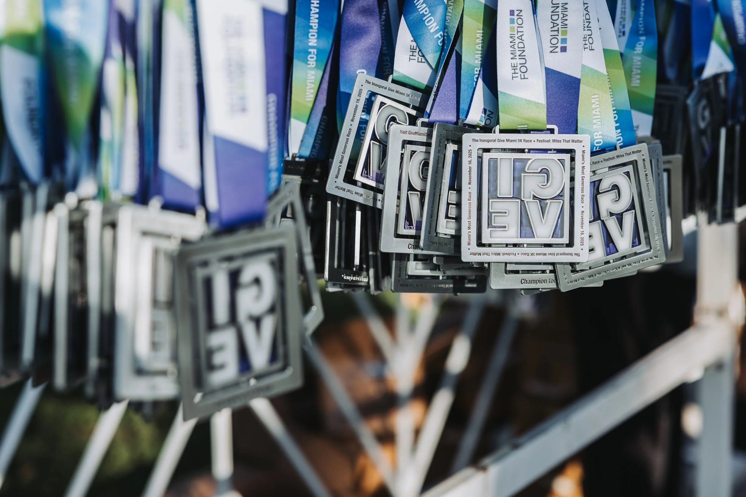A display of multiple medals with the word 'LOVE' in a square pattern, hanging from a rack next to blue and green event flyers.