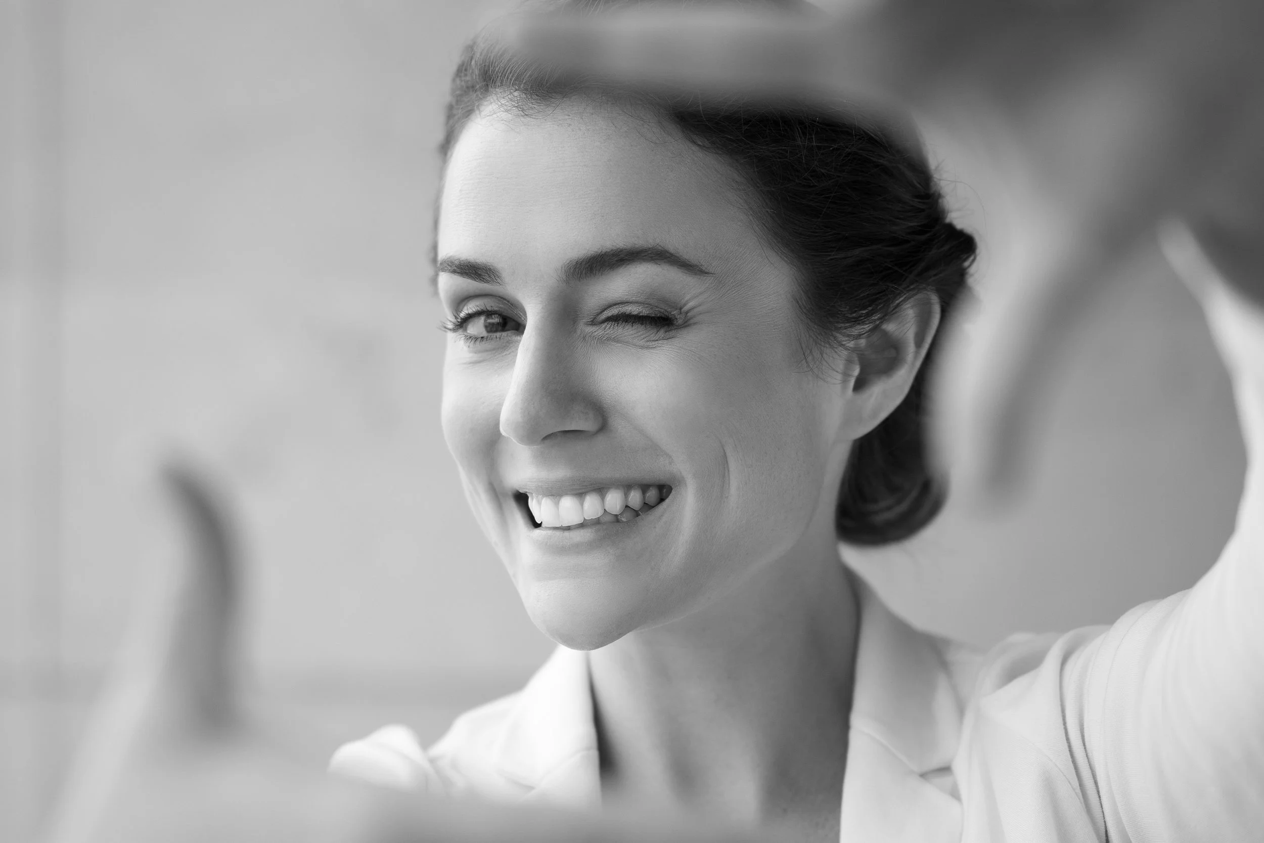 A woman taking a selfie, smiling with one eye closed, in black and white.