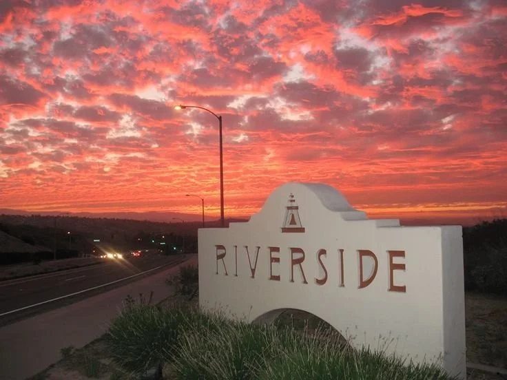 Sunset with colorful clouds behind a Welcome to Riverside sign near the highway.