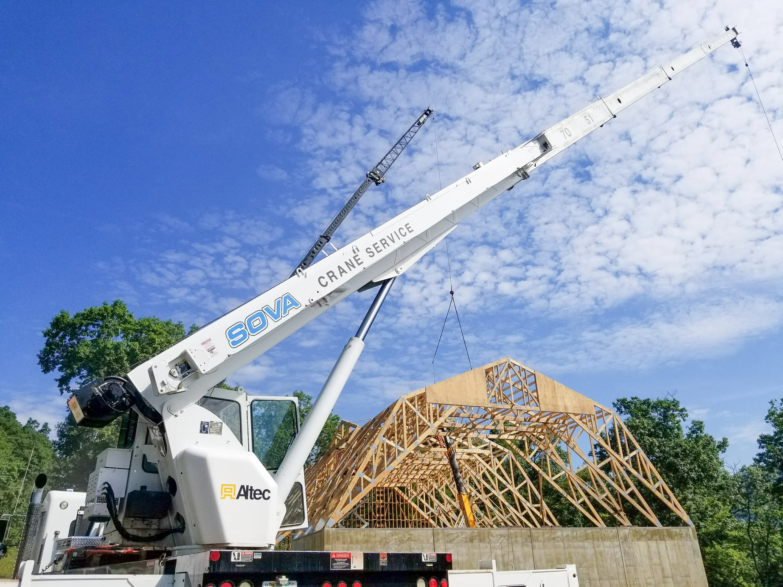 Construction crane lifting wooden framework on a building under construction with a blue sky and some clouds.