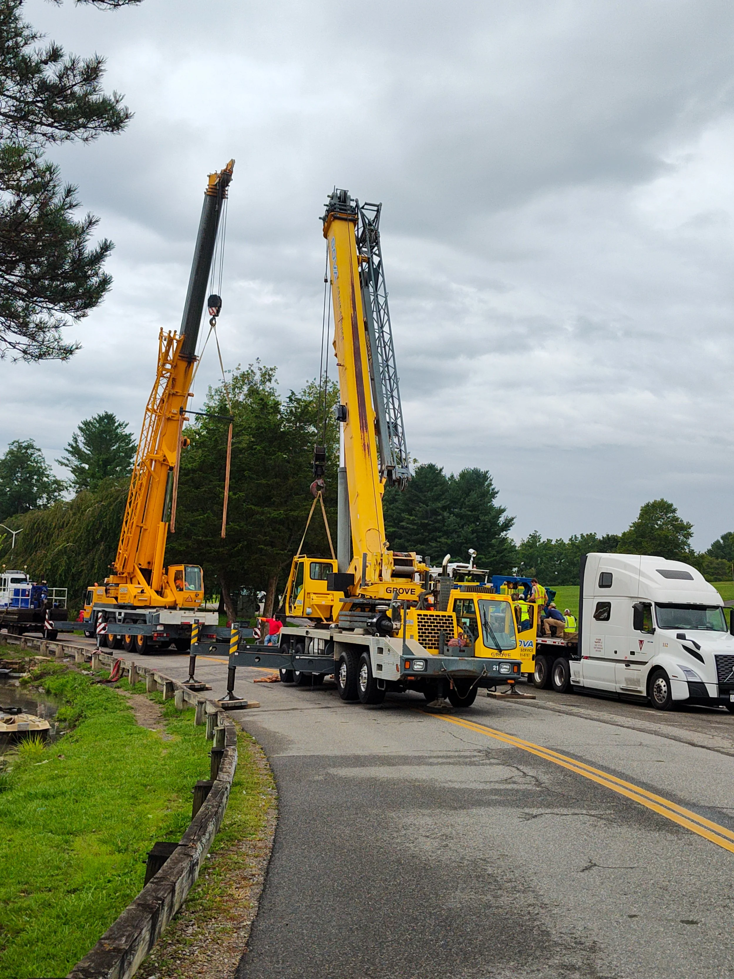 Two large yellow cranes lifting and working on a road repair project on a cloudy day.