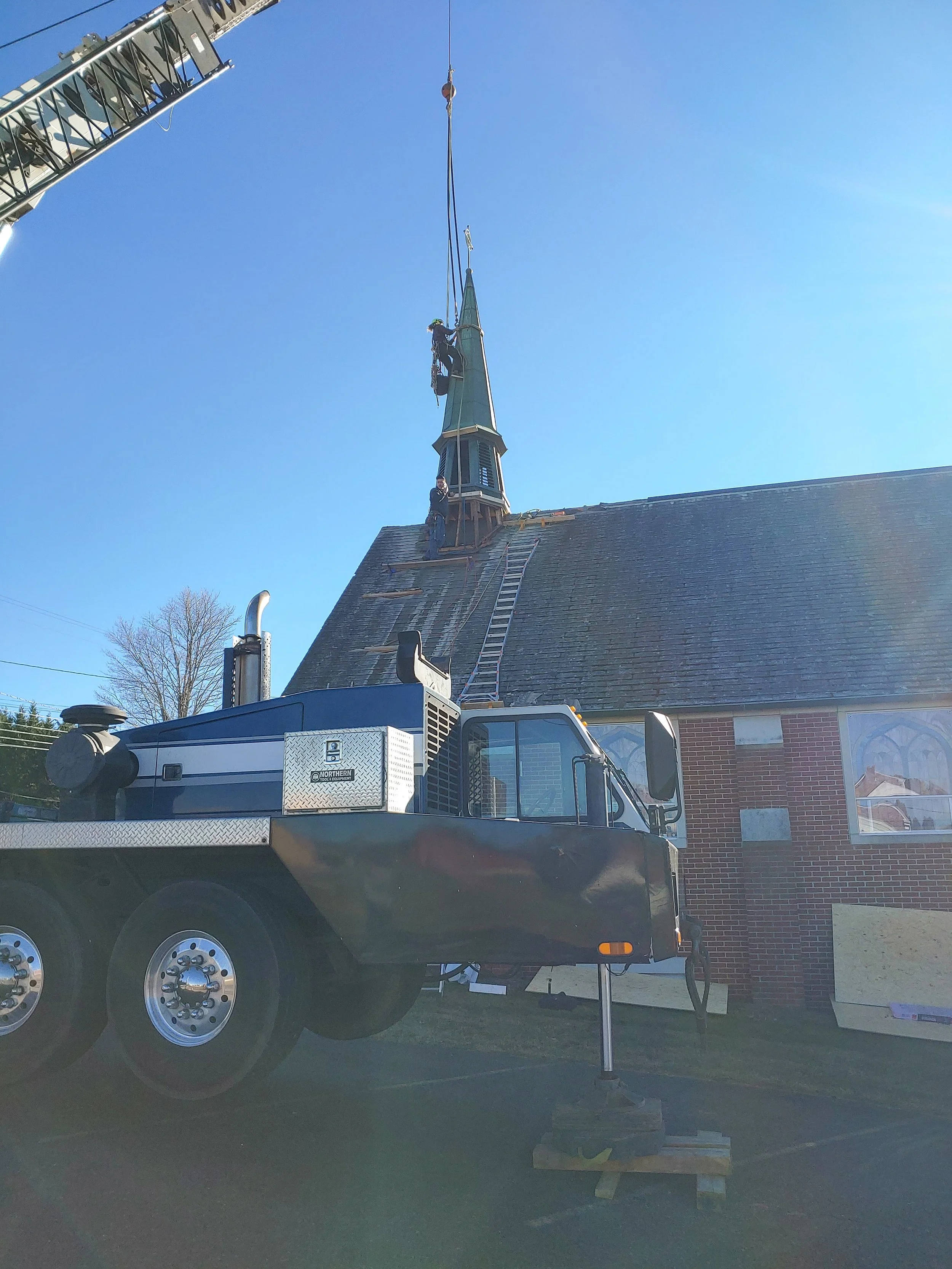 Workers on a crane repairing or cleaning the steeple of a church building.