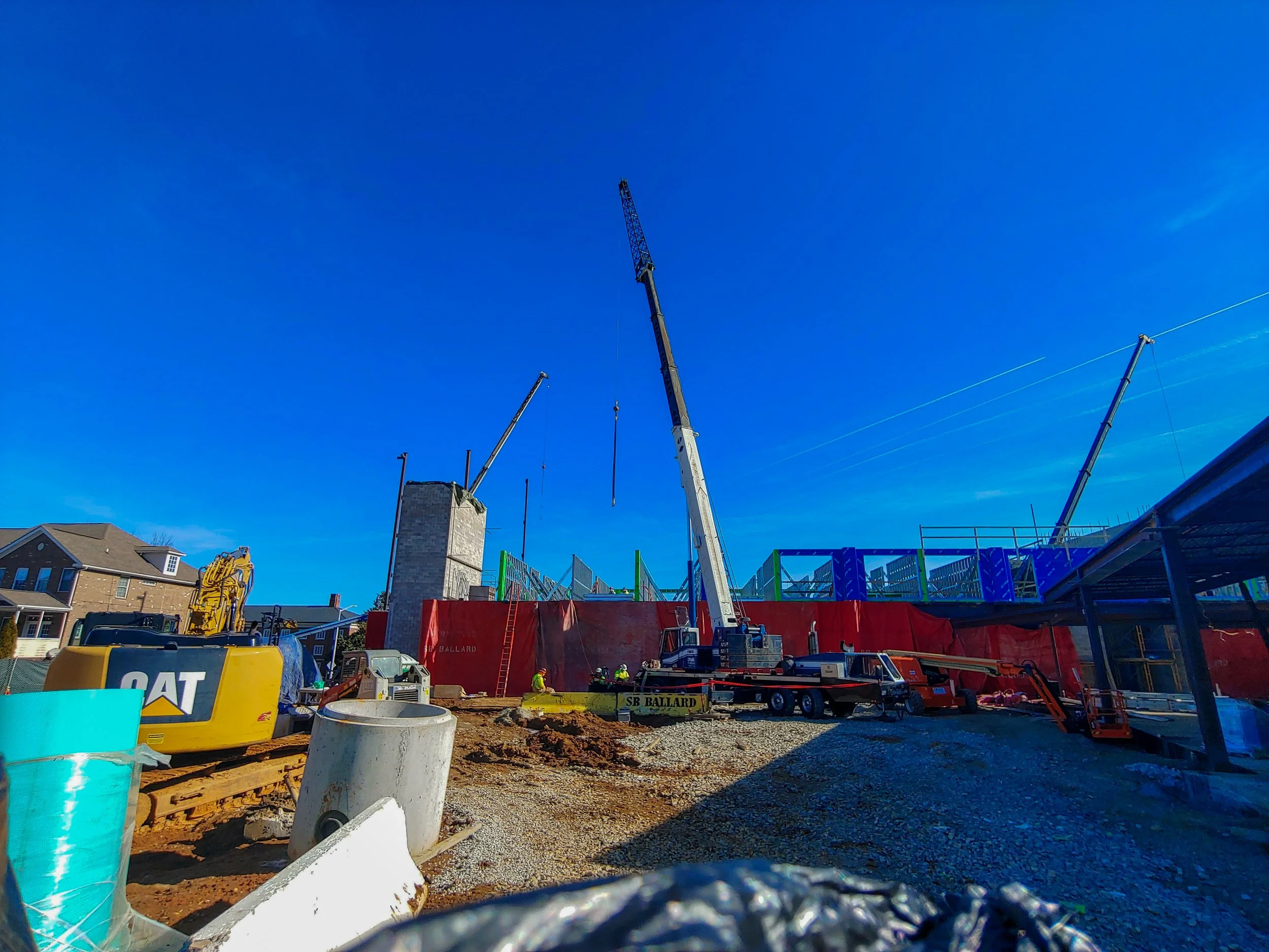 Construction site with cranes, construction vehicles, and a partially built structure under a clear blue sky.