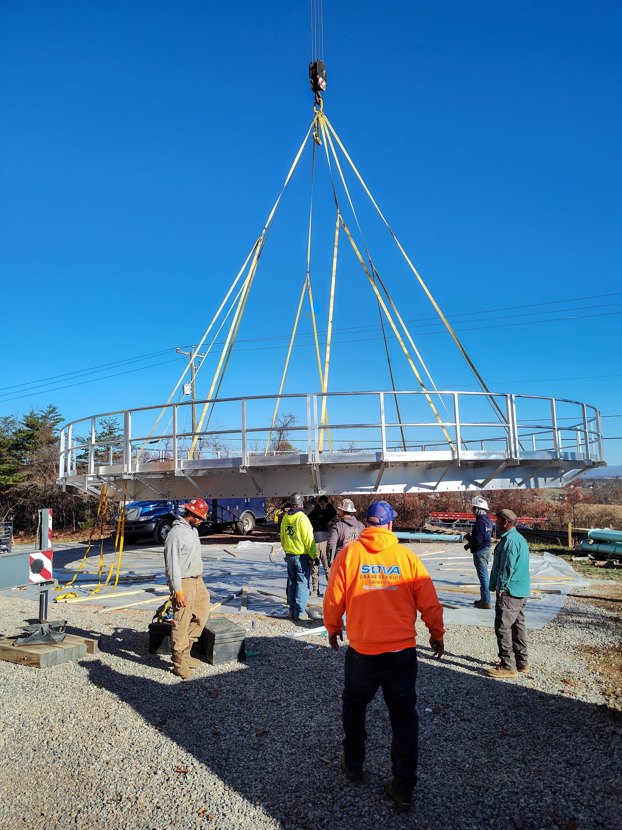 Construction workers assemble a large amusement park ride, which is being lifted into place by a crane.