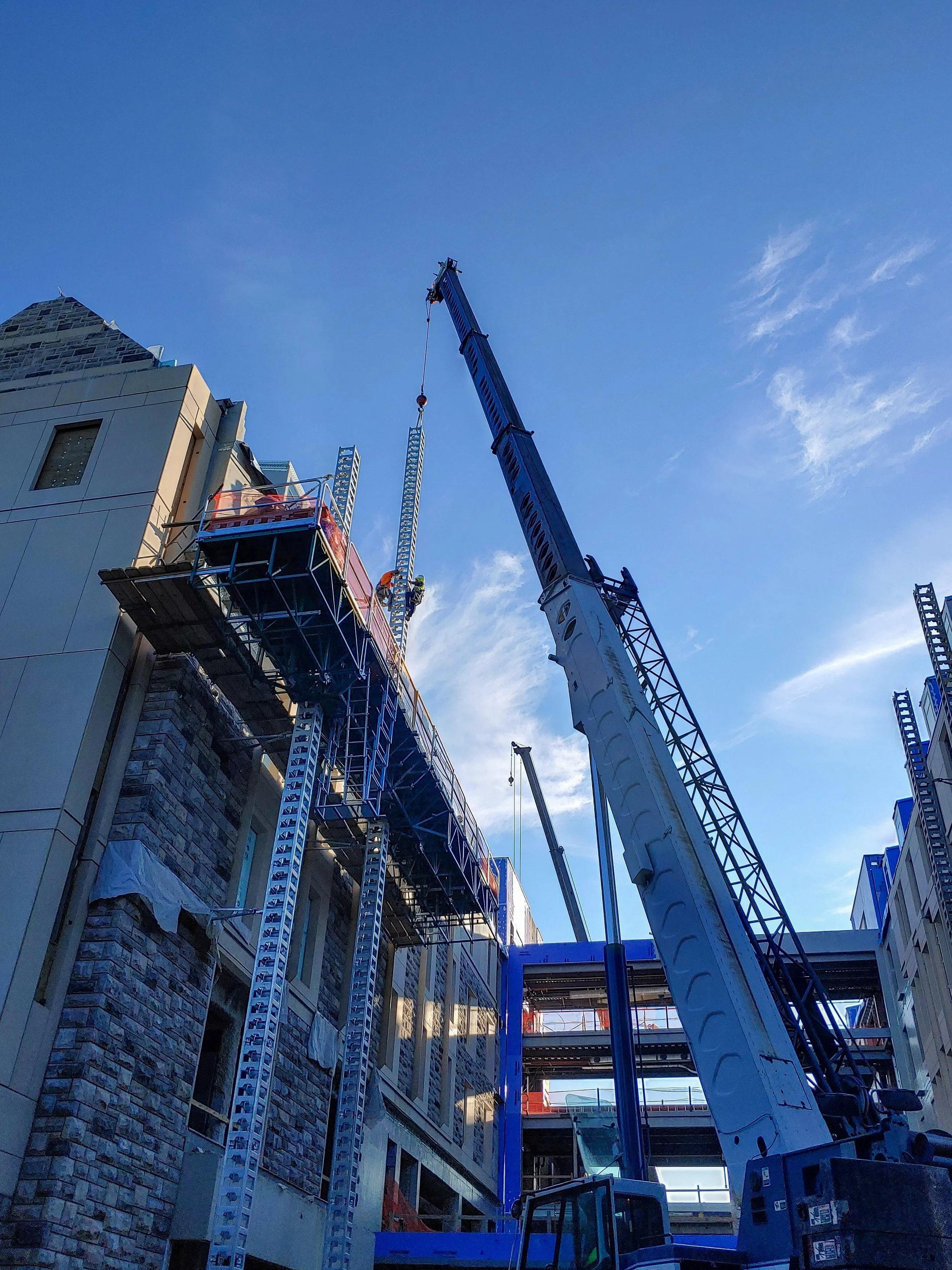 Construction site with a large crane lifting materials and workers on scaffolding on an urban building against a clear blue sky.