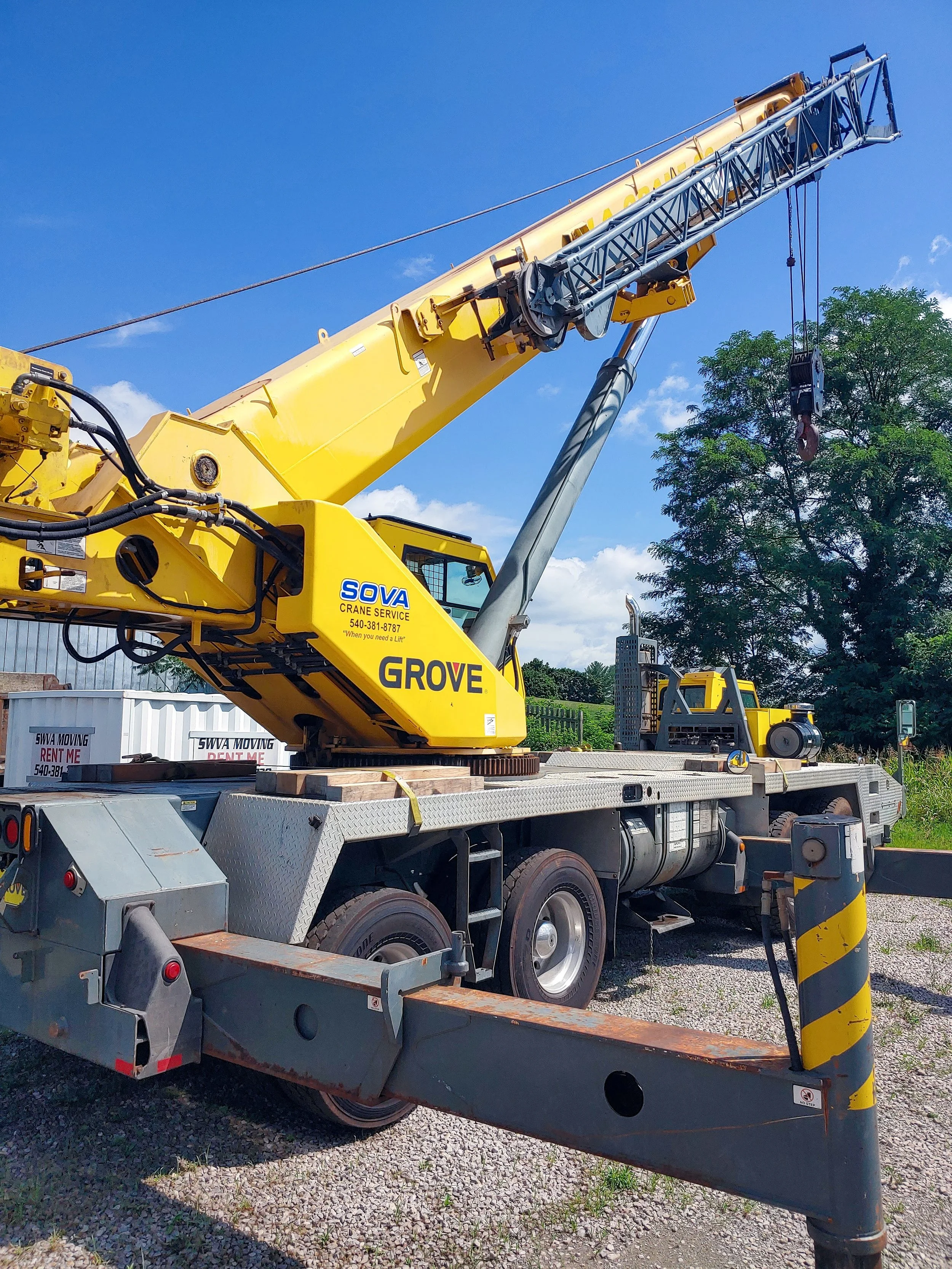 Yellow Grove crane on a flatbed truck with a clear blue sky and trees in the background