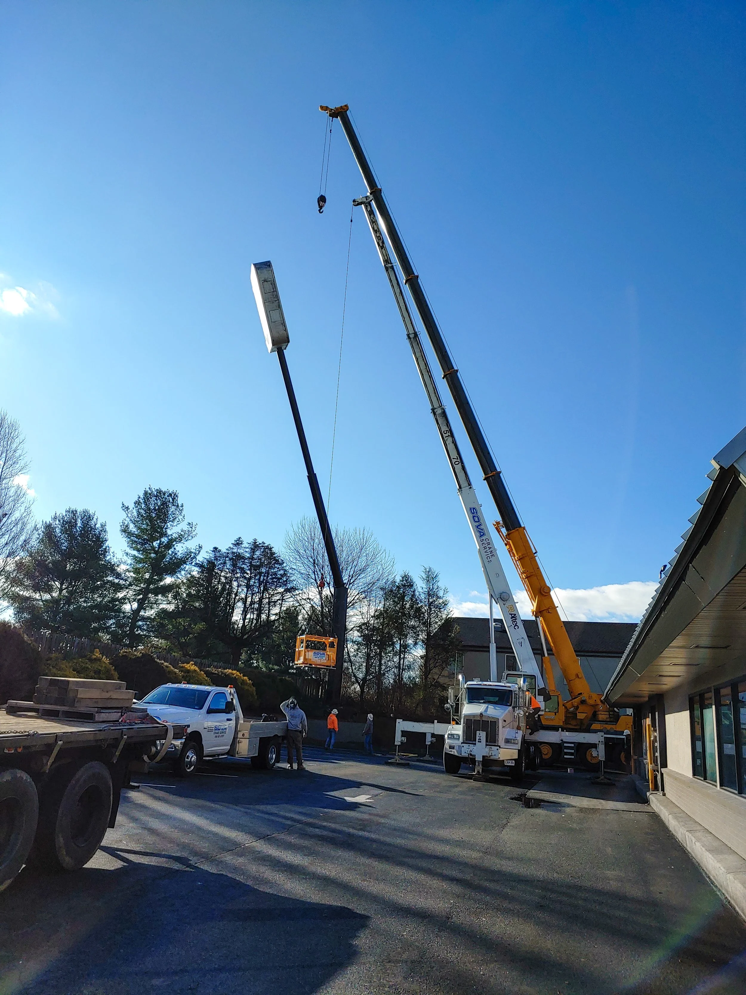 Workers using a crane to install a streetlight in a parking lot during daytime.