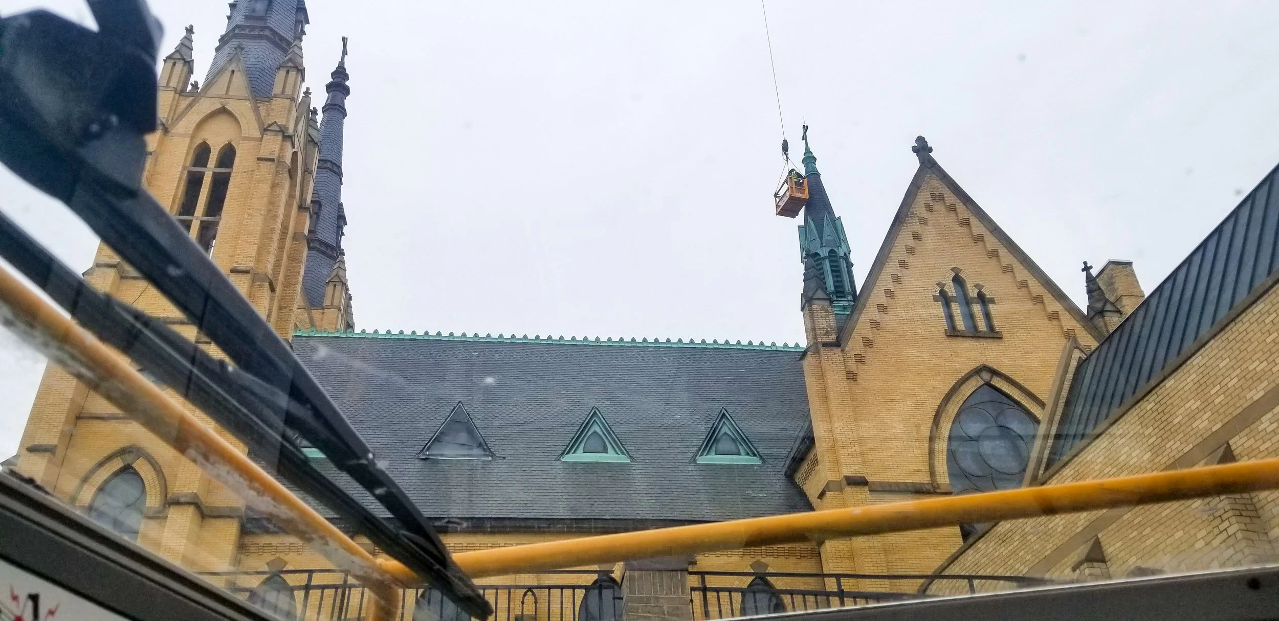 View of a historic church with pointed towers and stained glass windows, seen from below through a glass ceiling, with construction scaffolding and a lift in the area.