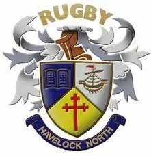 A military emblem featuring a shield with books, a helicopter, and a red cross on a yellow background. Above the shield is the word 'RUGBY,' and below is a banner with 'TRAVELOCK NORTH.' Gray decorative elements surround the shield.